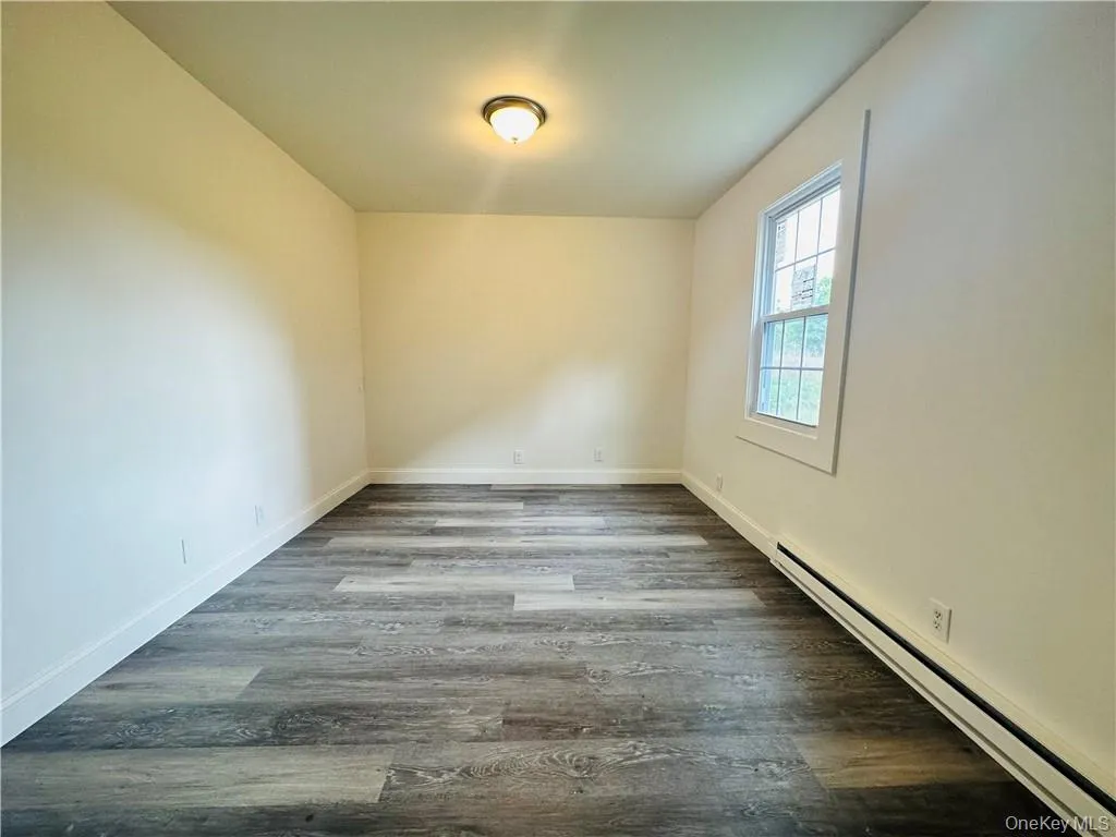 Unfurnished room featuring wood-type flooring and baseboard heating Unfurnished room featuring wood-type flooring and baseboard heating