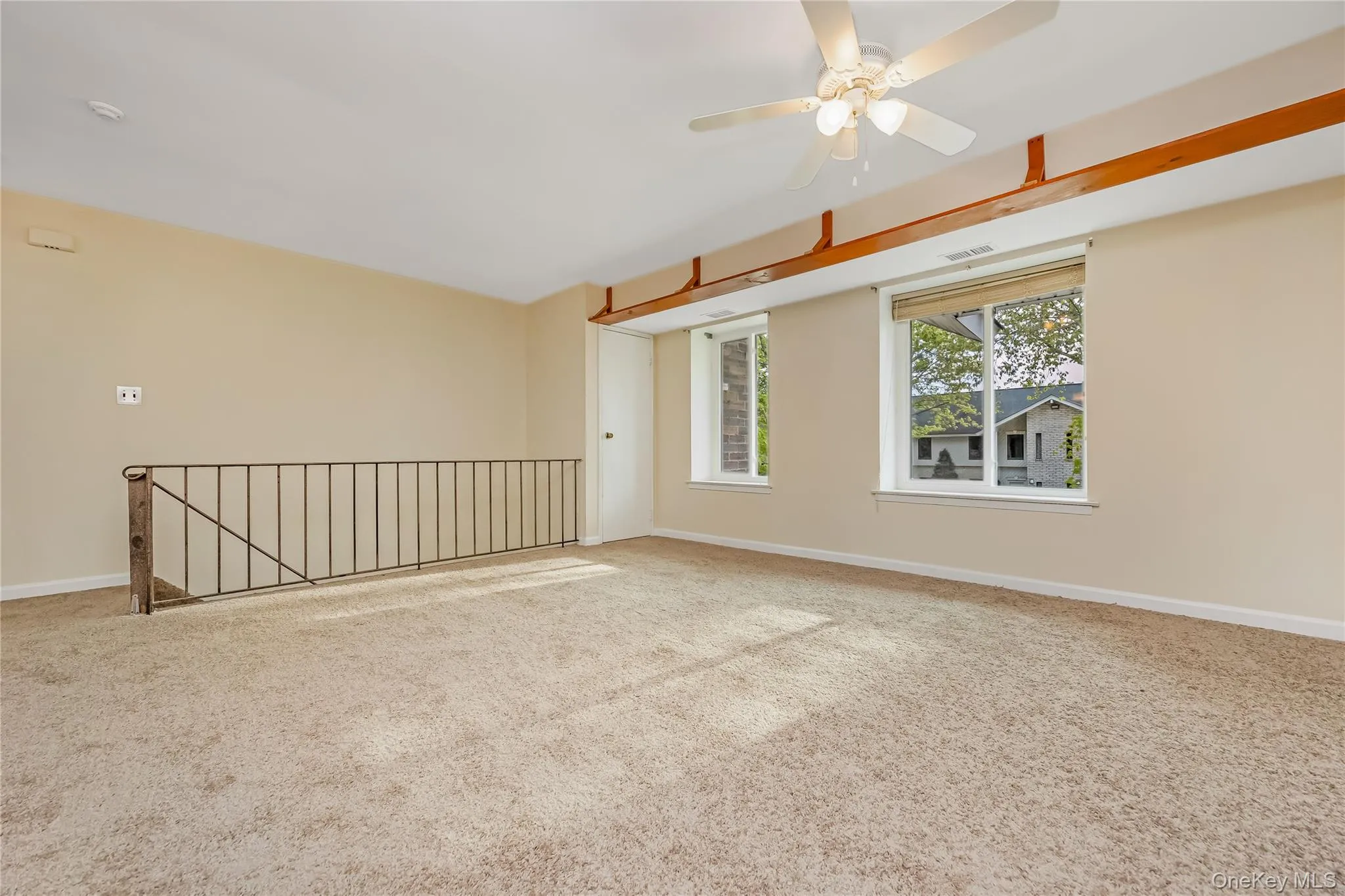 Spacious carpeted room featuring a ceiling fan, exposed wood shelving, windows, and a metal railing overlooking a lower level Spacious carpeted room featuring a ceiling fan, exposed wood shelving, windows, and a metal railing overlooking a lower level