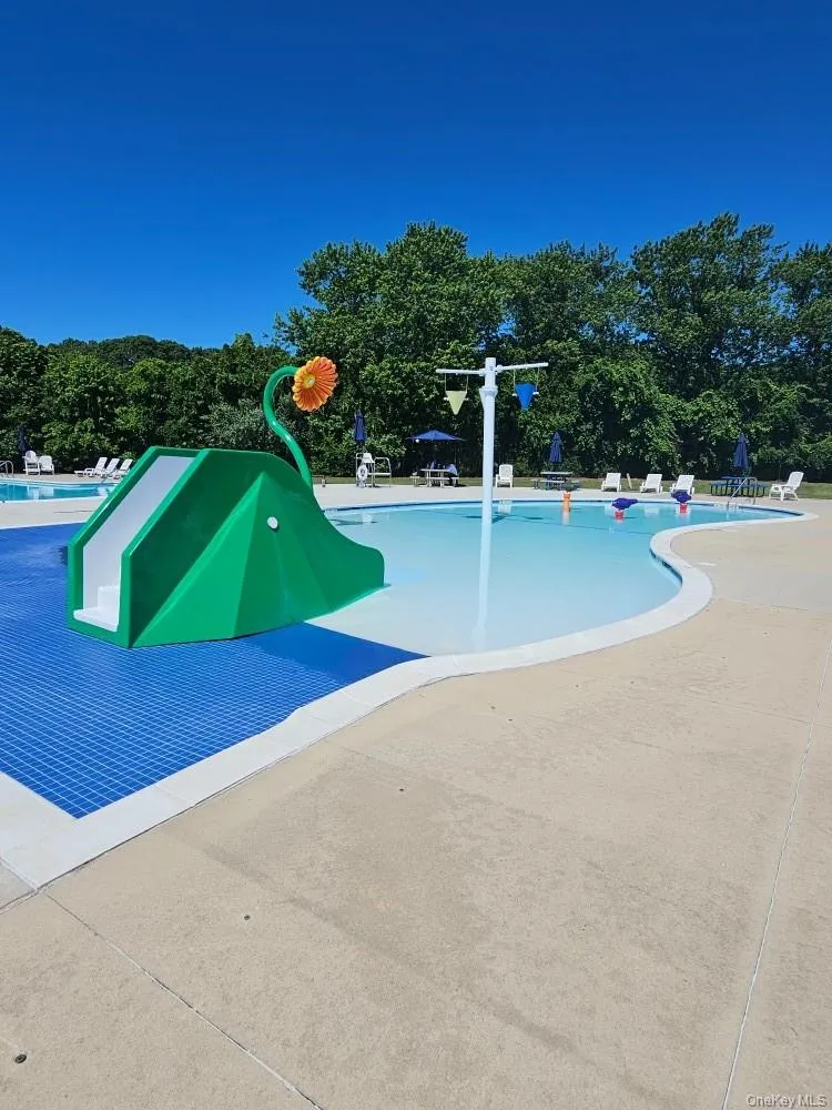Resort-style pool area featuring a water slide, splash pad with water features, and expansive concrete decking Resort-style pool area featuring a water slide, splash pad with water features, and expansive concrete decking
