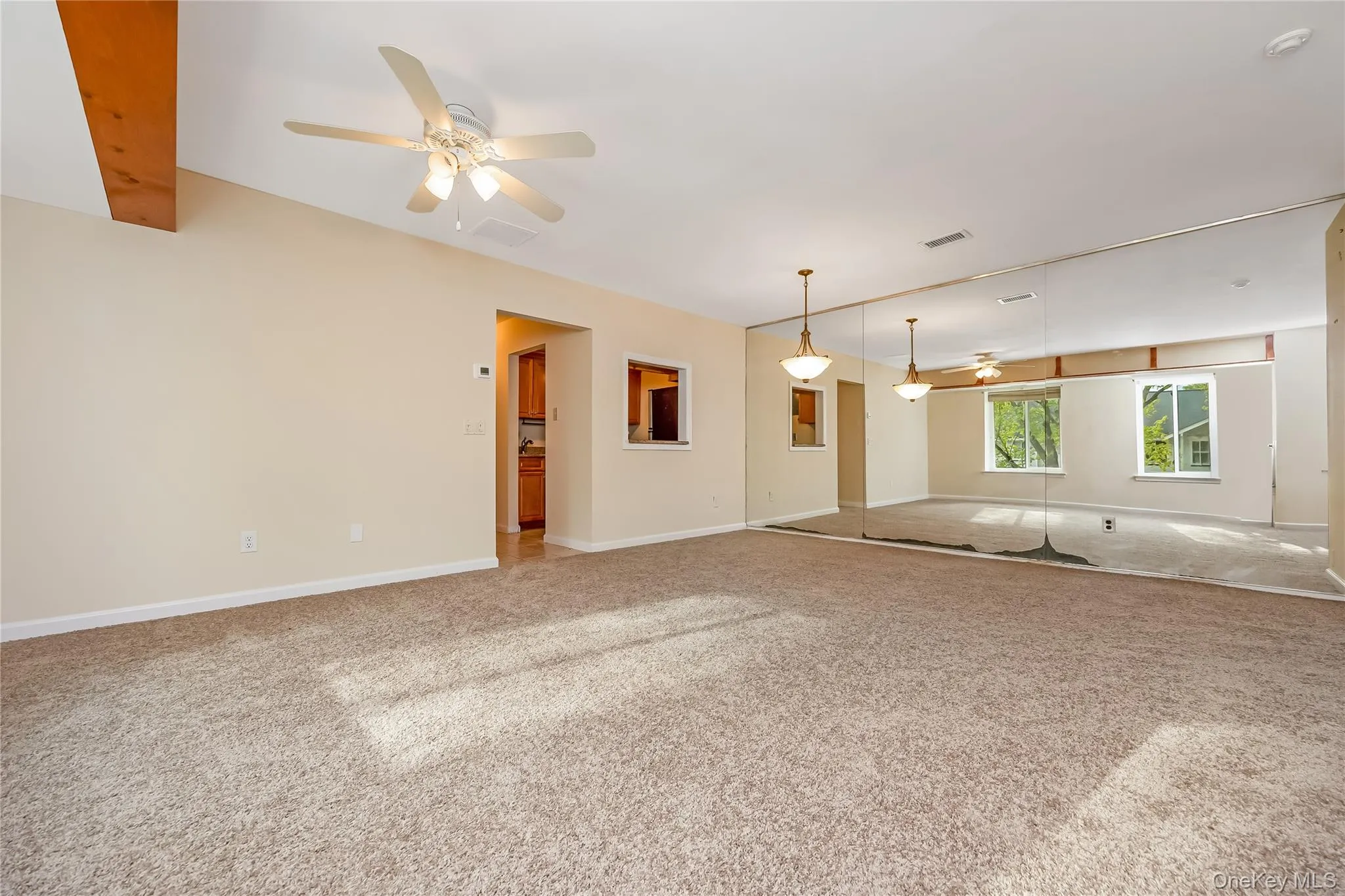 Spacious room featuring neutral carpeting, a full wall of mirrors, and a ceiling fan with light fixture Spacious room featuring neutral carpeting, a full wall of mirrors, and a ceiling fan with light fixture