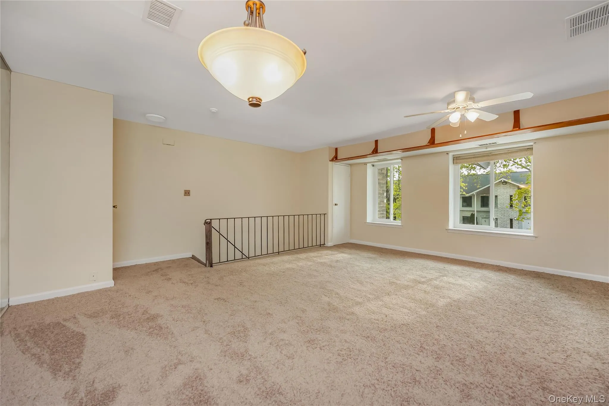 Spacious room featuring neutral carpet flooring, two windows, and a ceiling fan Spacious room featuring neutral carpet flooring, two windows, and a ceiling fan