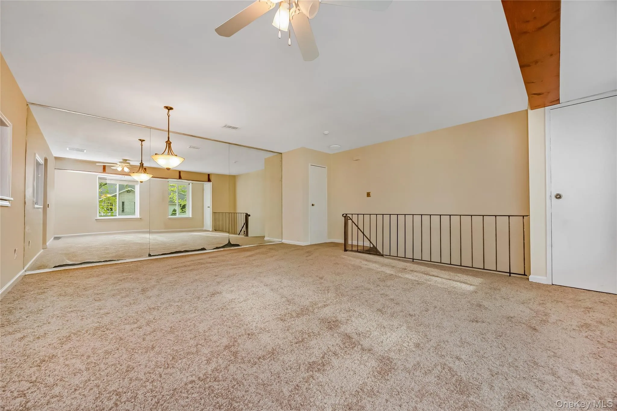 Spacious room featuring textured carpeting, extensive wall-mounted mirrors, and multiple ceiling fans Spacious room featuring textured carpeting, extensive wall-mounted mirrors, and multiple ceiling fans