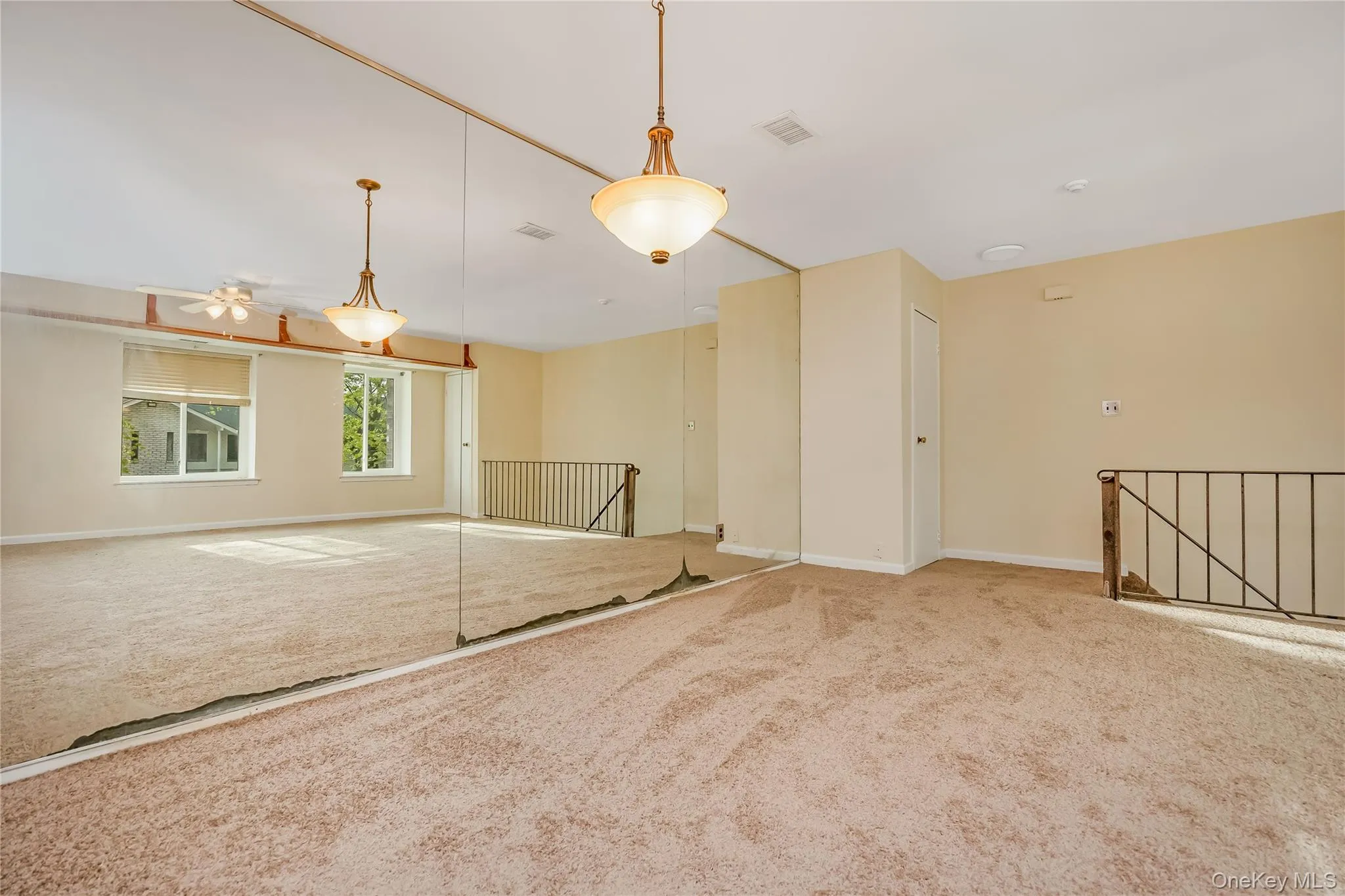 Carpeted open loft area featuring a full mirrored wall, two windows, two chandeliers, and a ceiling fan Carpeted open loft area featuring a full mirrored wall, two windows, two chandeliers, and a ceiling fan