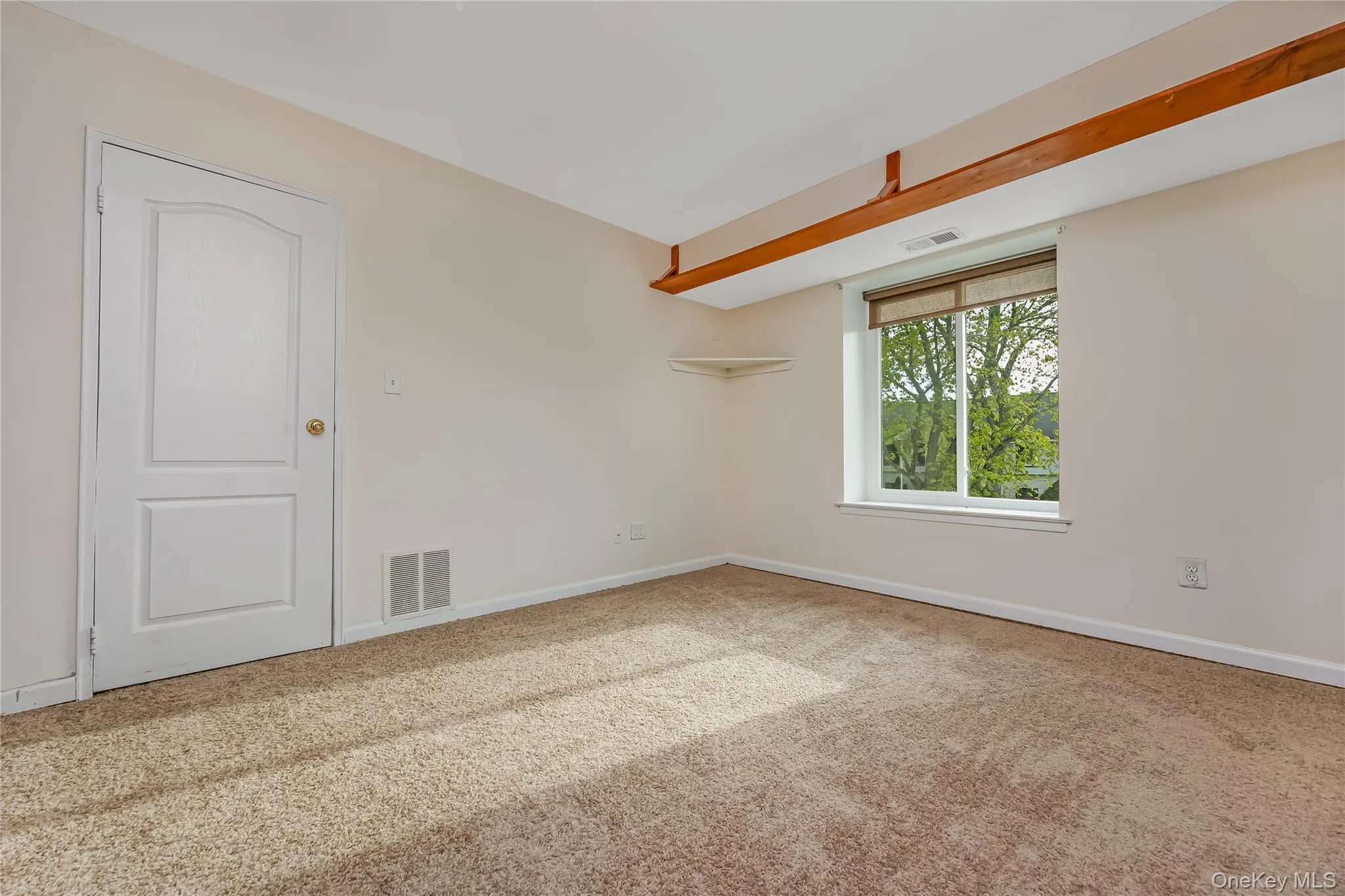 Carpeted room with a large window, featuring exposed wood shelving & a Large walk-in closet. Carpeted room with a large window, featuring exposed wood shelving & a Large walk-in closet.