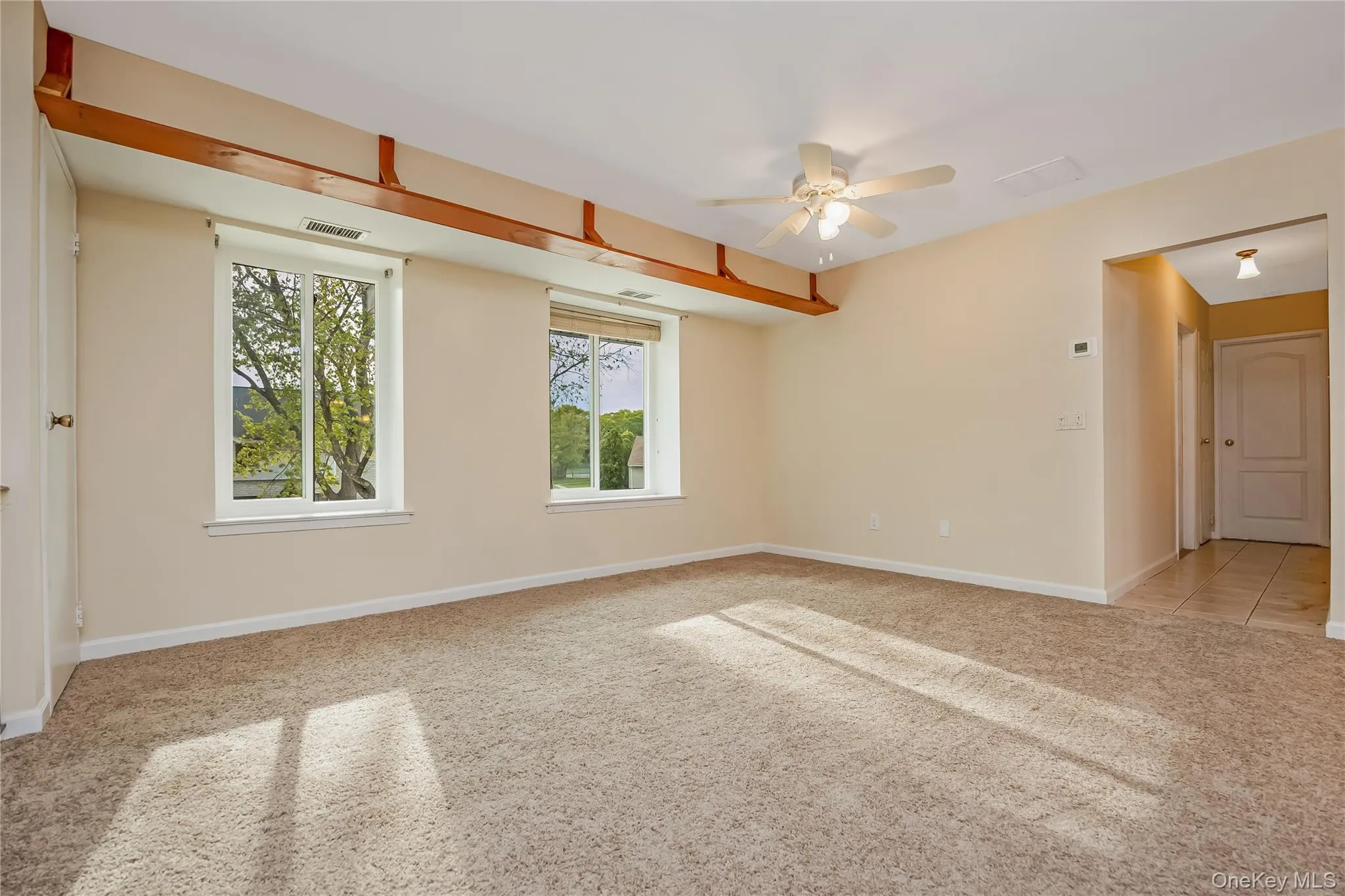 Spacious room featuring neutral carpeting, two windows with blinds, wood shelving, a ceiling fan with integrated lighting. Spacious room featuring neutral carpeting, two windows with blinds, wood shelving, a ceiling fan with integrated lighting.