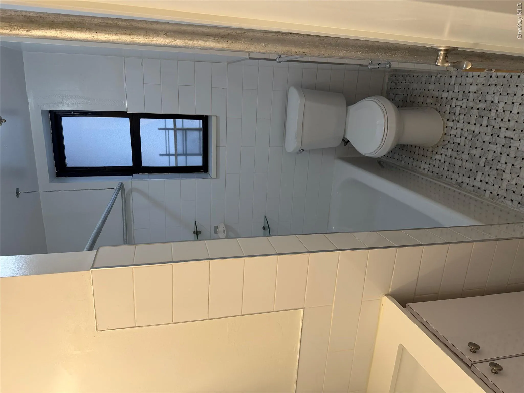Bathroom featuring subway tile walls, a built-in bathtub, and a window with a dark frame Bathroom featuring subway tile walls, a built-in bathtub, and a window with a dark frame