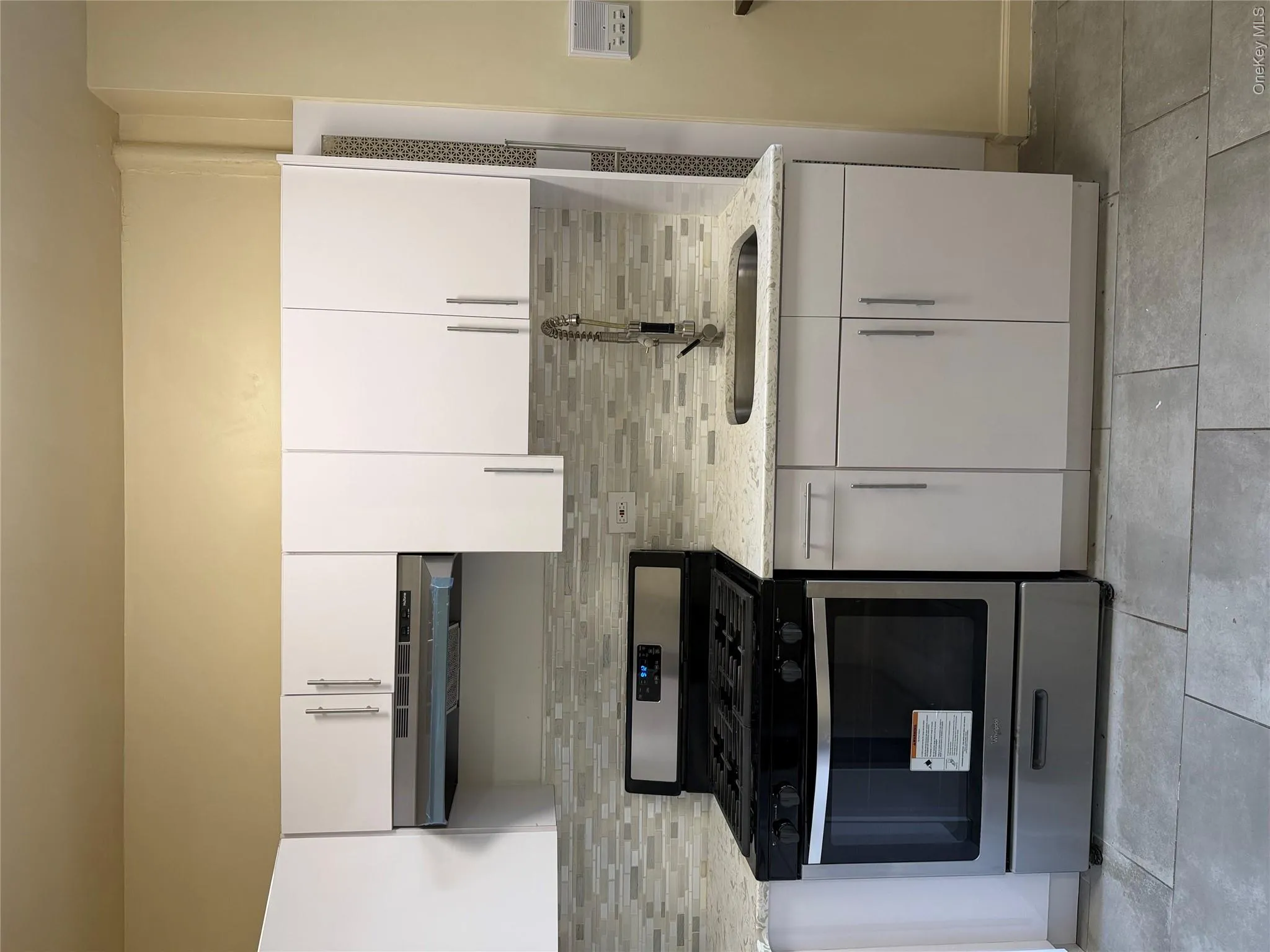 Kitchen featuring white cabinetry, light-colored countertops, stainless steel appliances, a tile backsplash, and light gray floor tiles Kitchen featuring white cabinetry, light-colored countertops, stainless steel appliances, a tile backsplash, and light gray floor tiles