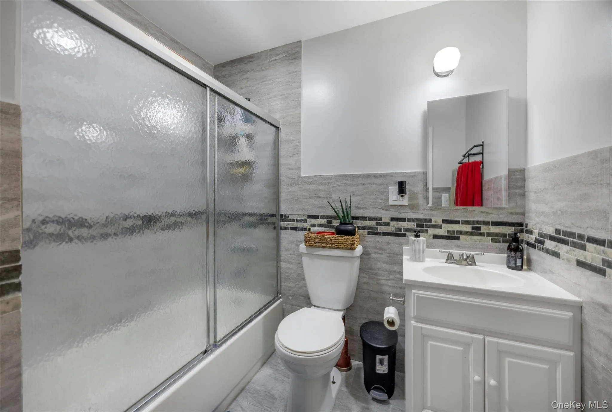 Bathroom with vanity, enclosed tub / shower combo, tile walls, and a wainscoted wall Bathroom with vanity, enclosed tub / shower combo, tile walls, and a wainscoted wall