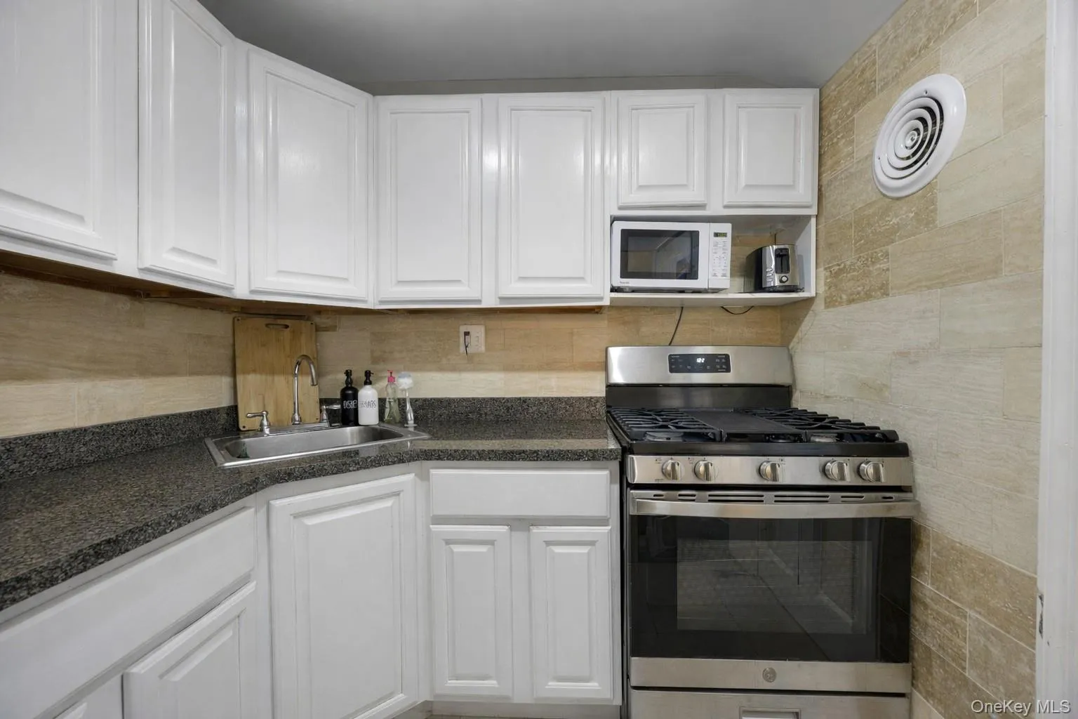 Kitchen featuring gas stove, white cabinets, white microwave, and tasteful backsplash Kitchen featuring gas stove, white cabinets, white microwave, and tasteful backsplash