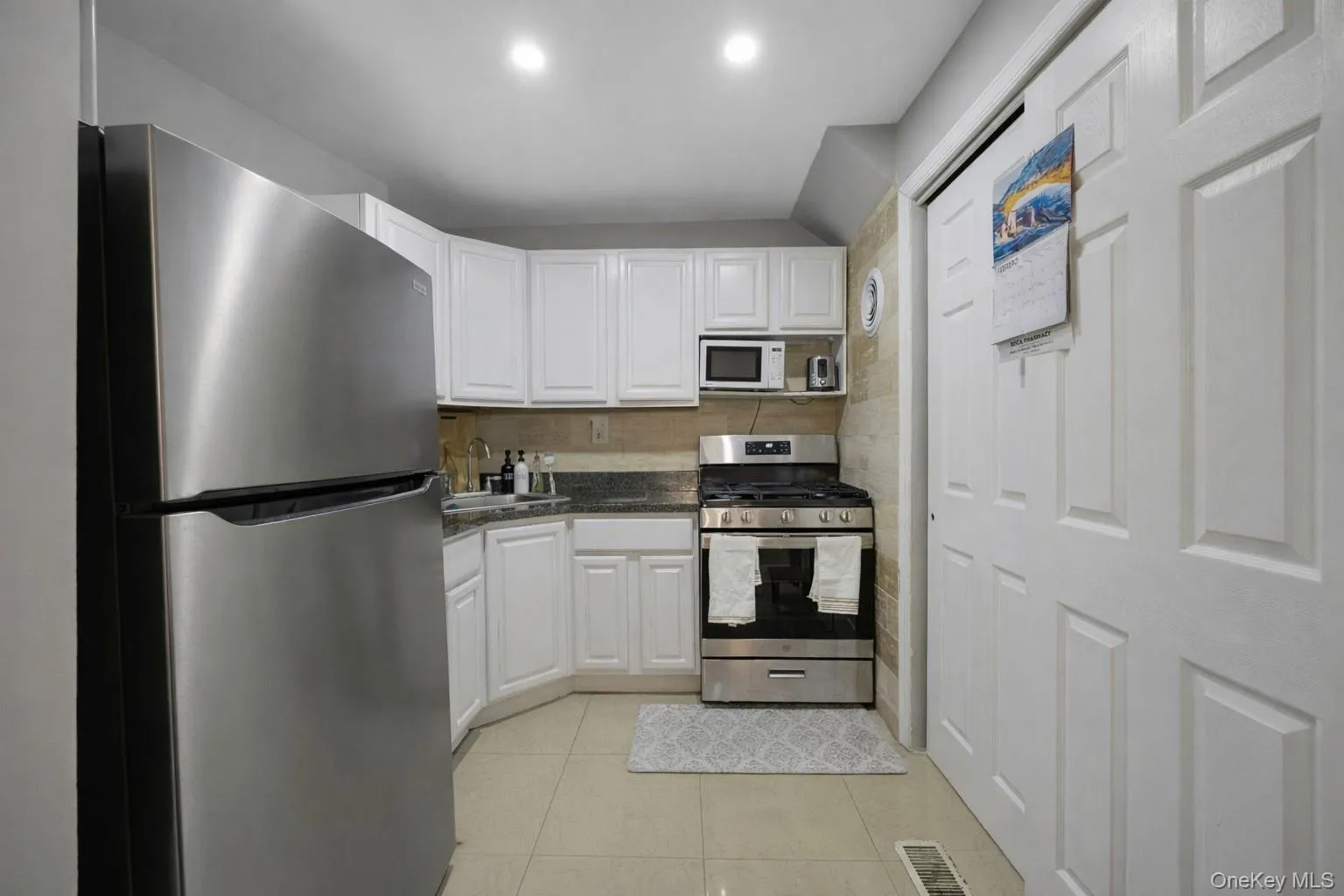 Kitchen with stainless steel appliances, white cabinetry, light tile patterned flooring, and dark stone counters Kitchen with stainless steel appliances, white cabinetry, light tile patterned flooring, and dark stone counters