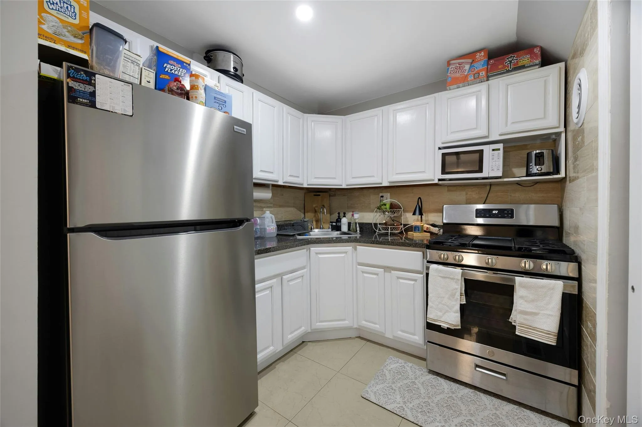 Kitchen featuring stainless steel appliances, white cabinetry, light tile patterned flooring, dark stone countertops, and backsplash Kitchen featuring stainless steel appliances, white cabinetry, light tile patterned flooring, dark stone countertops, and backsplash