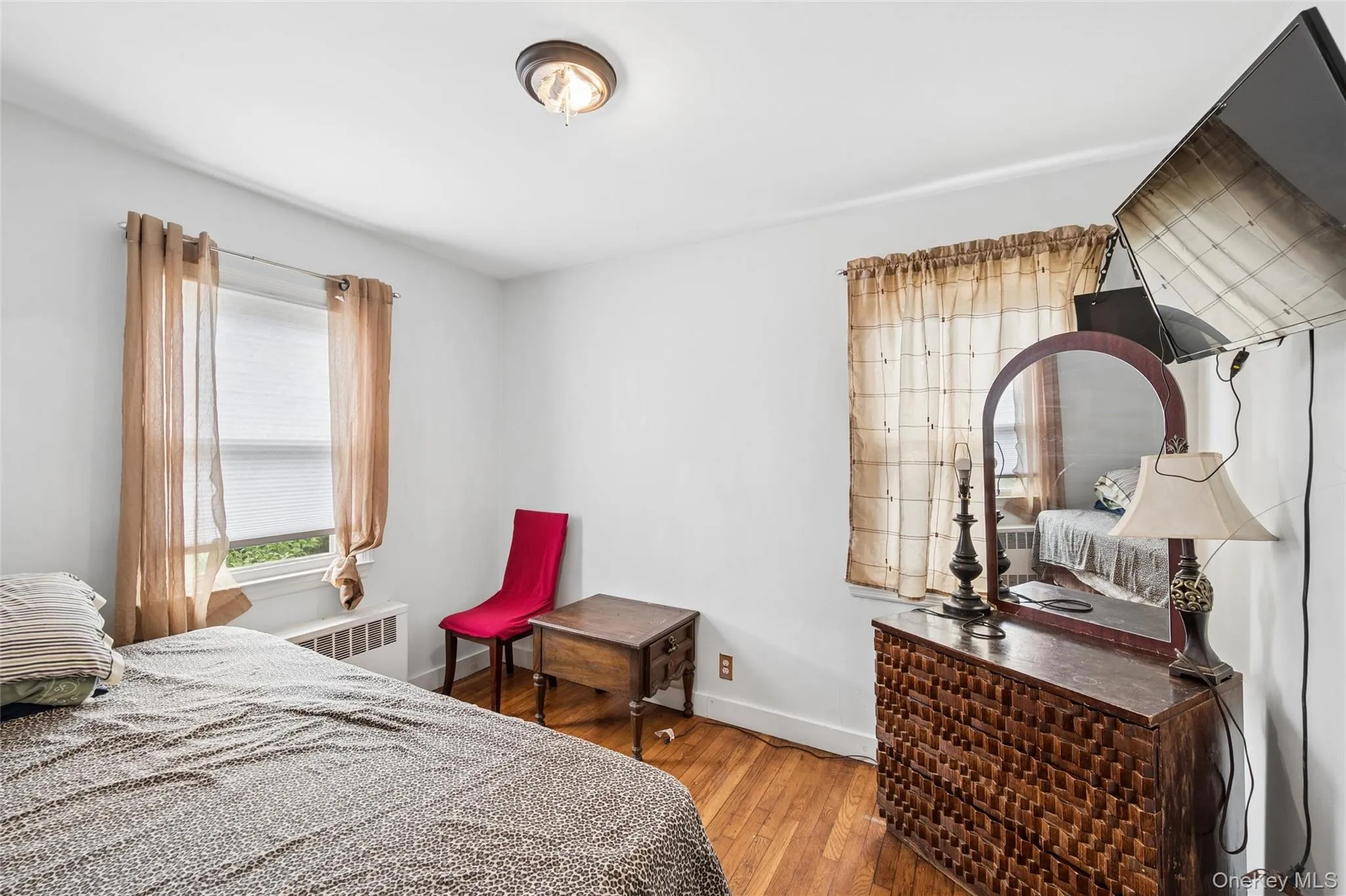 Bright interior space featuring a window with blinds, wood-finish flooring, and a ceiling-mounted light fixture Bright interior space featuring a window with blinds, wood-finish flooring, and a ceiling-mounted light fixture