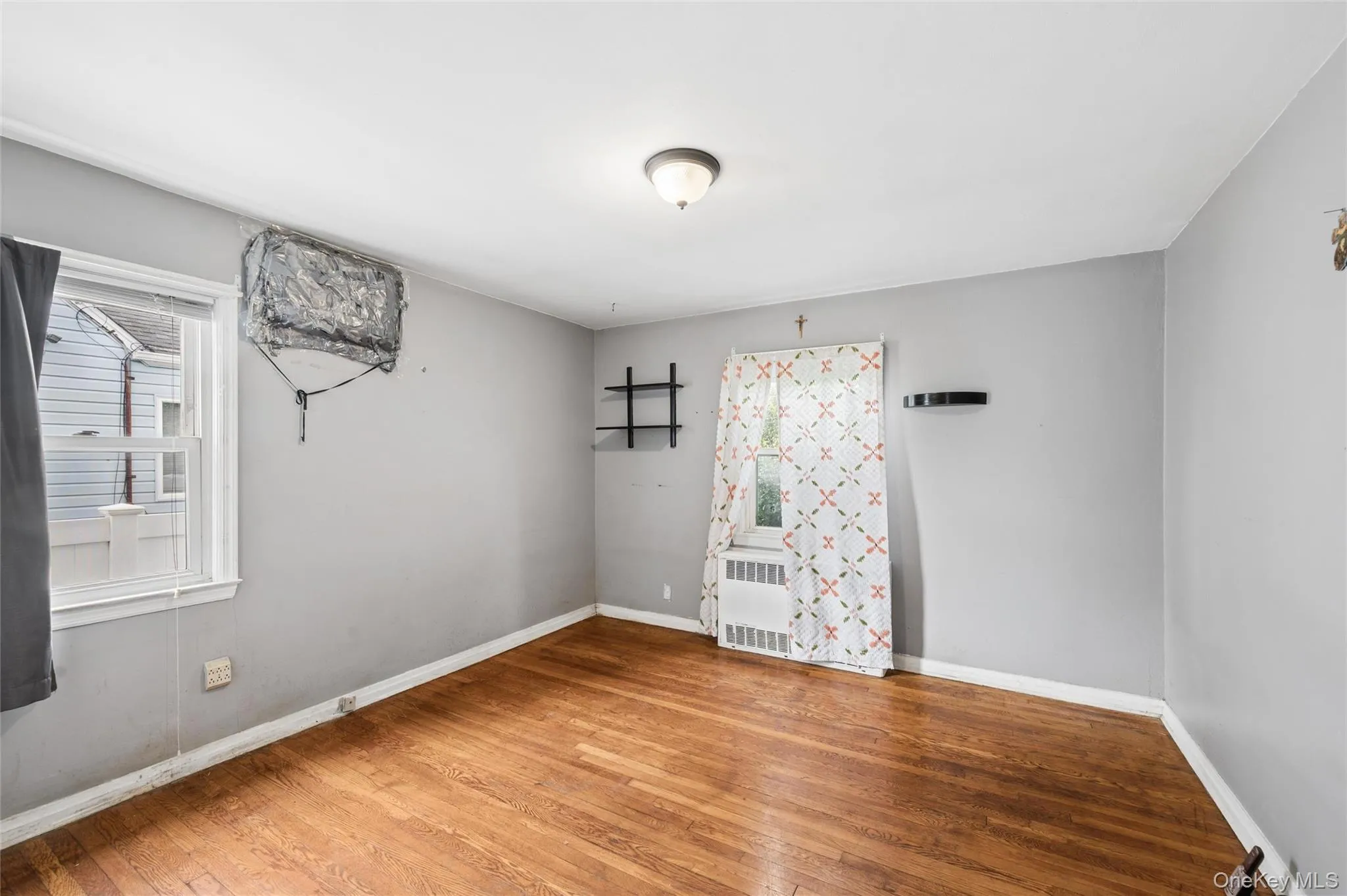 Hardwood flooring and light gray walls define this room, featuring a window-mounted air conditioning unit and baseboard heating Hardwood flooring and light gray walls define this room, featuring a window-mounted air conditioning unit and baseboard heating