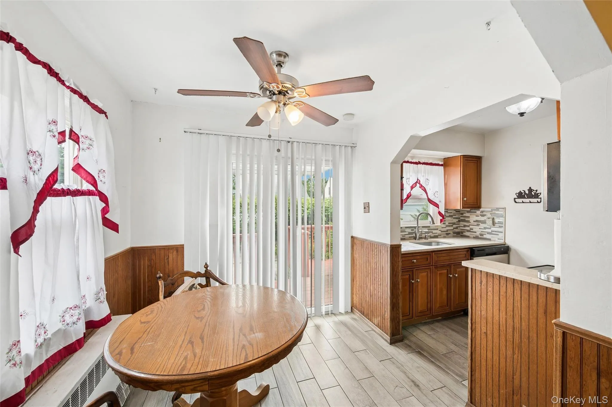 Dining area featuring wood-finish flooring, half-wall wainscoting, and a ceiling fan with integrated lighting Dining area featuring wood-finish flooring, half-wall wainscoting, and a ceiling fan with integrated lighting
