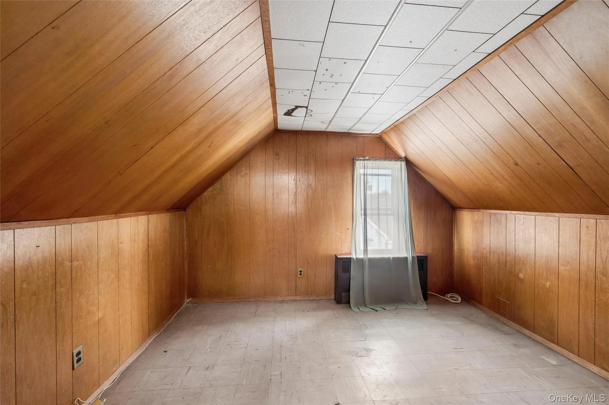 Attic space featuring wood paneling on walls and ceiling, a window, and an exposed radiator Attic space featuring wood paneling on walls and ceiling, a window, and an exposed radiator