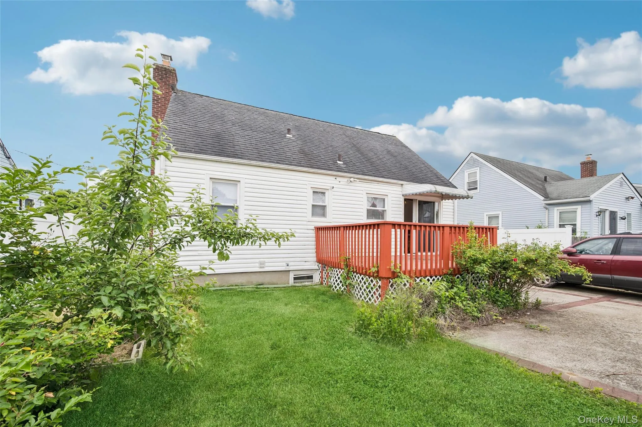 Rear exterior featuring white horizontal siding, a red-stained wooden deck with lattice skirting, and a manicured lawn Rear exterior featuring white horizontal siding, a red-stained wooden deck with lattice skirting, and a manicured lawn
