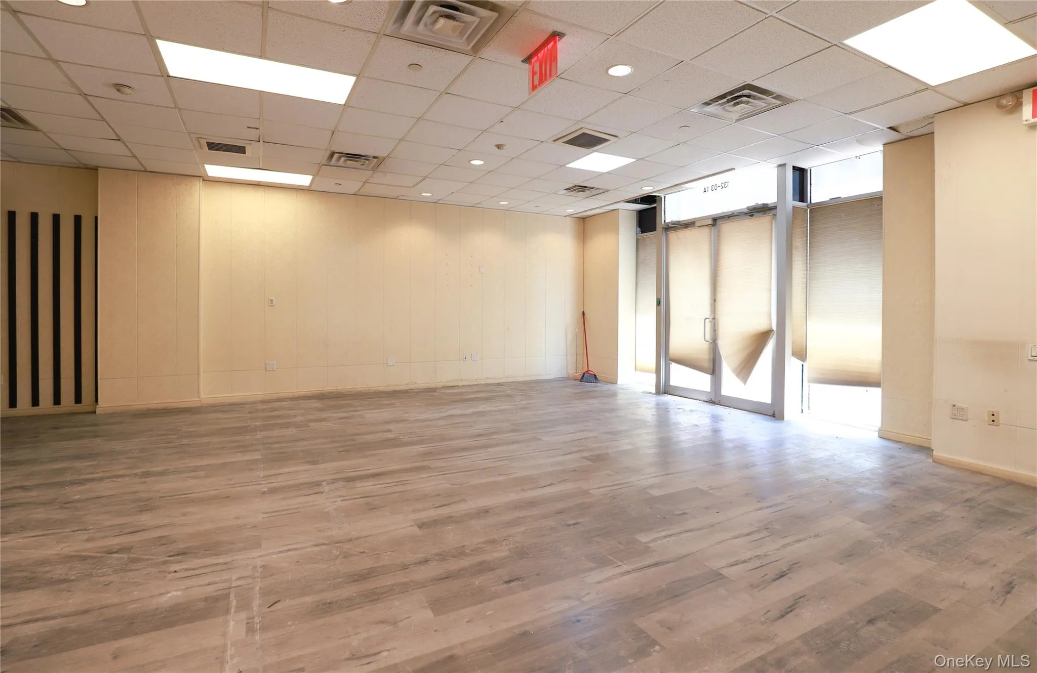 Expansive interior space featuring wood-finish flooring, drop ceiling with recessed lighting, and large storefront windows with roller shades Expansive interior space featuring wood-finish flooring, drop ceiling with recessed lighting, and large storefront windows with roller shades