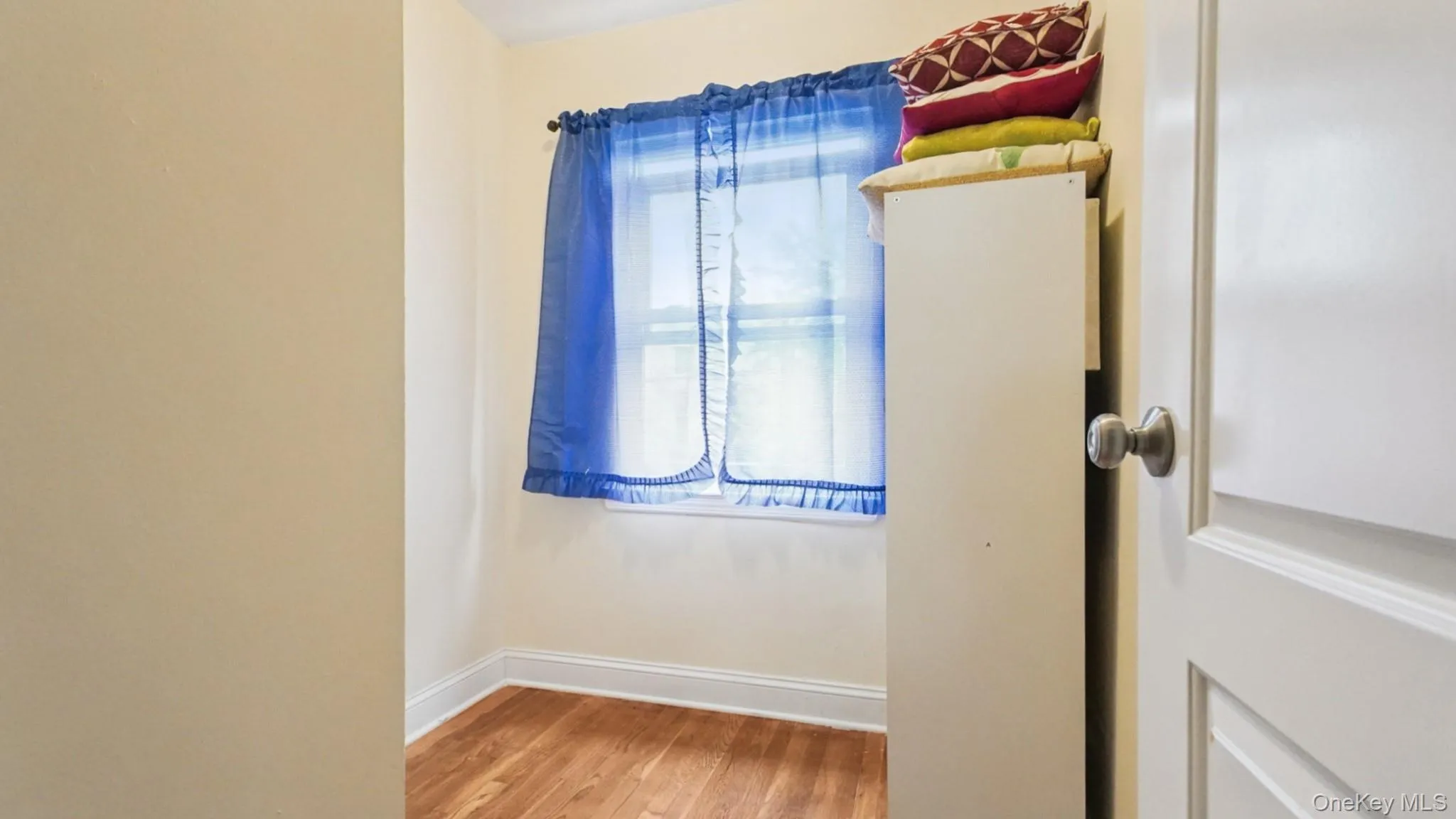 Room featuring wood-finish flooring, light-toned wall paint, and white baseboards Room featuring wood-finish flooring, light-toned wall paint, and white baseboards