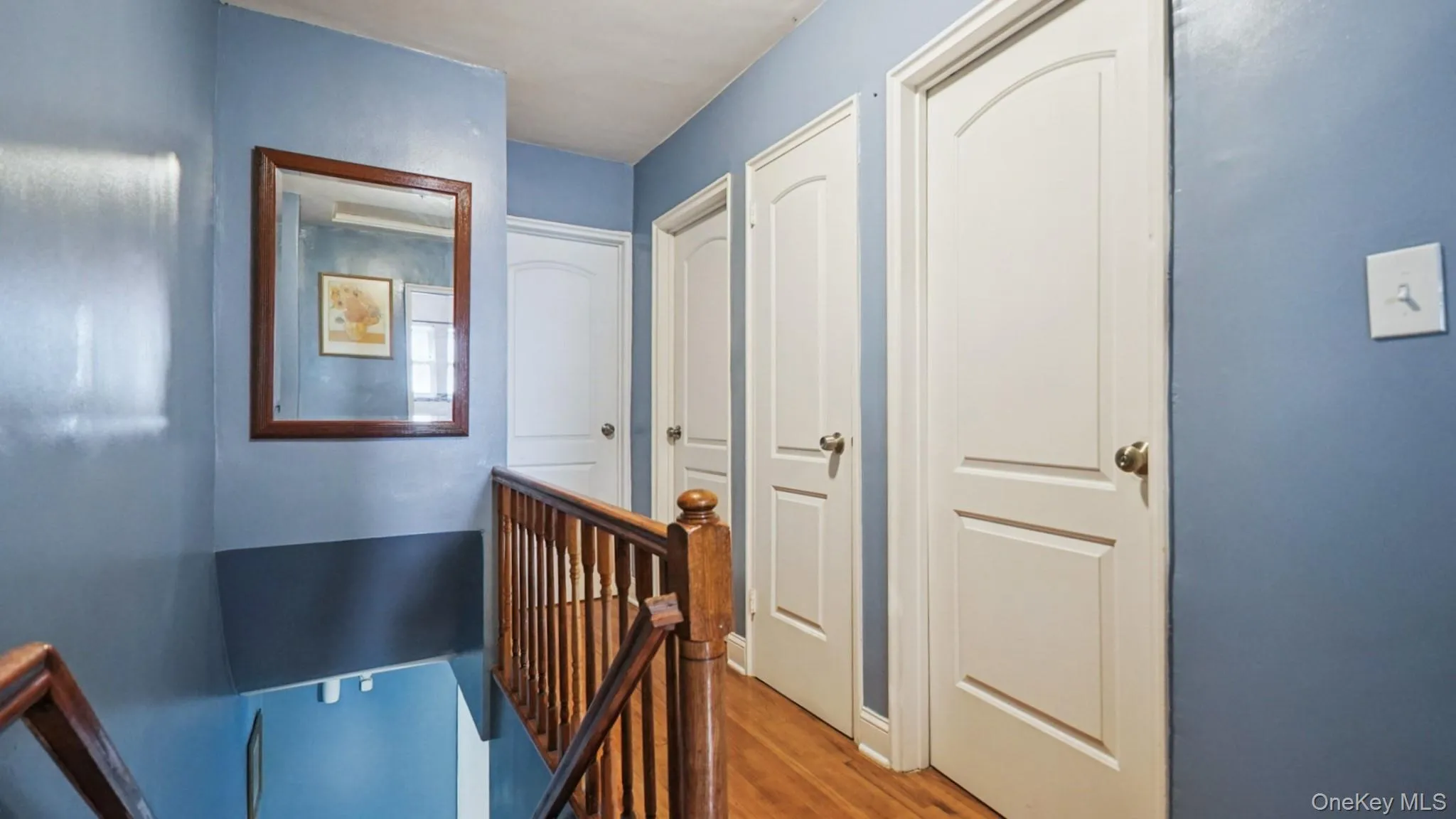 Hallway featuring wood-finish flooring, two-panel interior doors, and a wood banister Hallway featuring wood-finish flooring, two-panel interior doors, and a wood banister