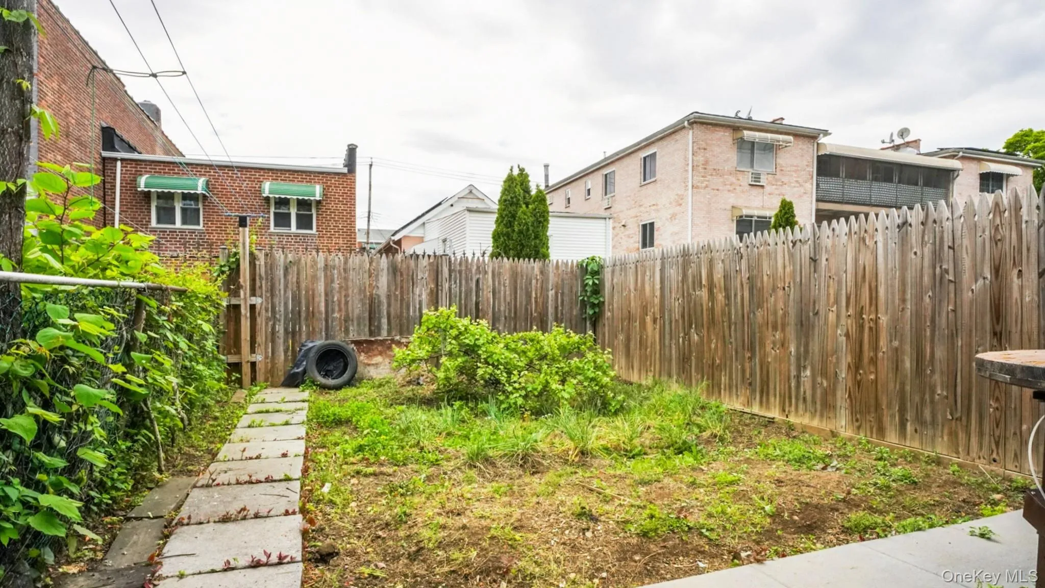 Expansive fenced backyard featuring a concrete patio section, a stone paver pathway, and mature perimeter foliage Expansive fenced backyard featuring a concrete patio section, a stone paver pathway, and mature perimeter foliage