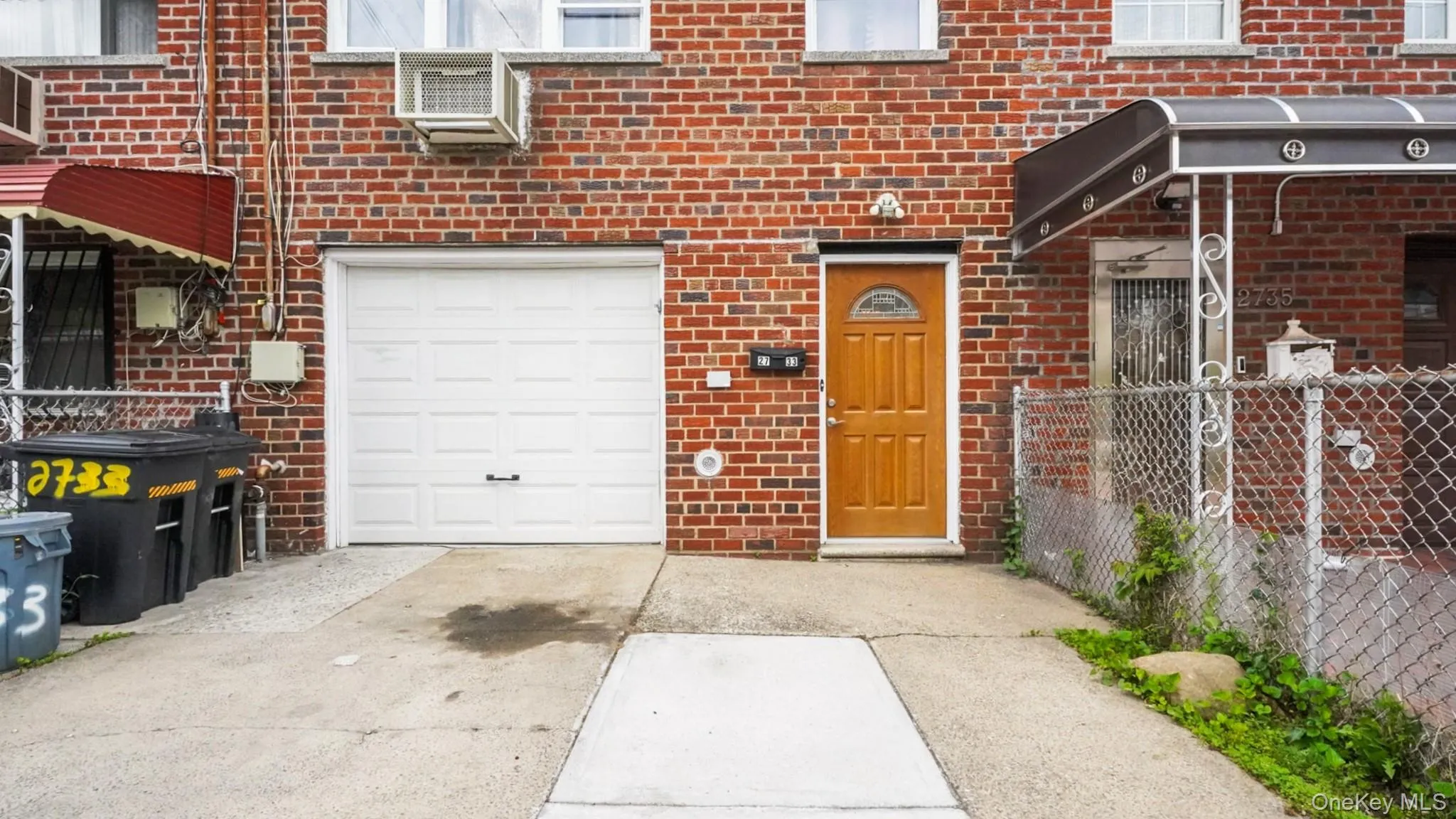 Brick facade featuring a panel garage door, light wood-finish entry door, and a concrete driveway Brick facade featuring a panel garage door, light wood-finish entry door, and a concrete driveway