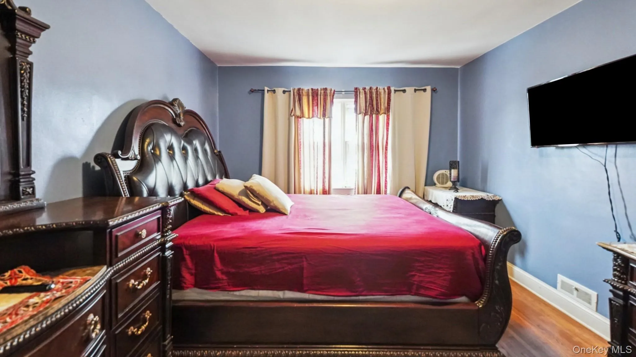 Bedroom featuring wood-finish flooring, a wall-mounted television, and baseboard registers Bedroom featuring wood-finish flooring, a wall-mounted television, and baseboard registers