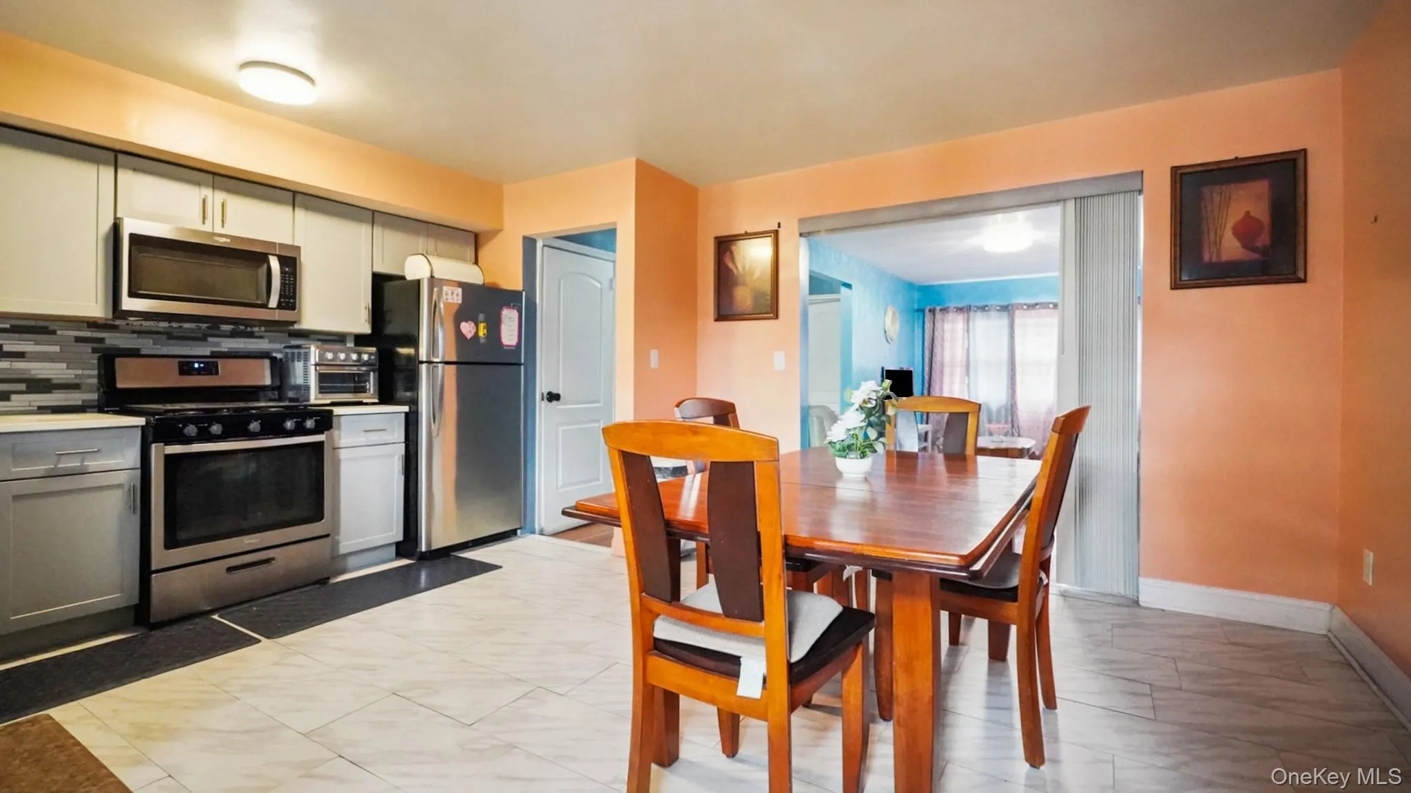 Kitchen and dining area featuring light gray cabinetry, stainless steel appliances, a gray mosaic tile backsplash, and light-toned floor tiling Kitchen and dining area featuring light gray cabinetry, stainless steel appliances, a gray mosaic tile backsplash, and light-toned floor tiling