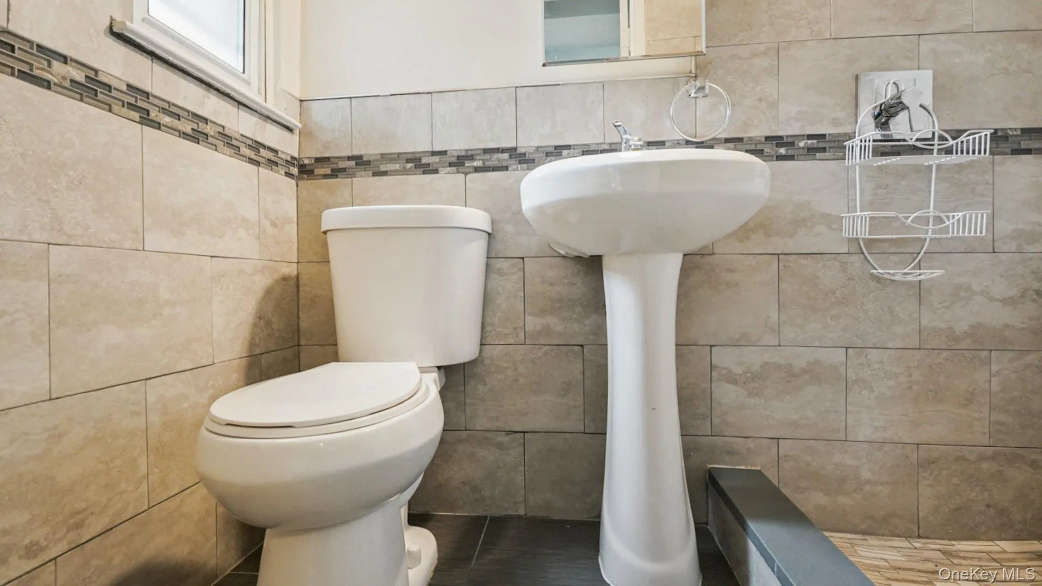 Bathroom featuring a white pedestal sink, toilet, and tiled walls with a decorative mosaic accent band Bathroom featuring a white pedestal sink, toilet, and tiled walls with a decorative mosaic accent band