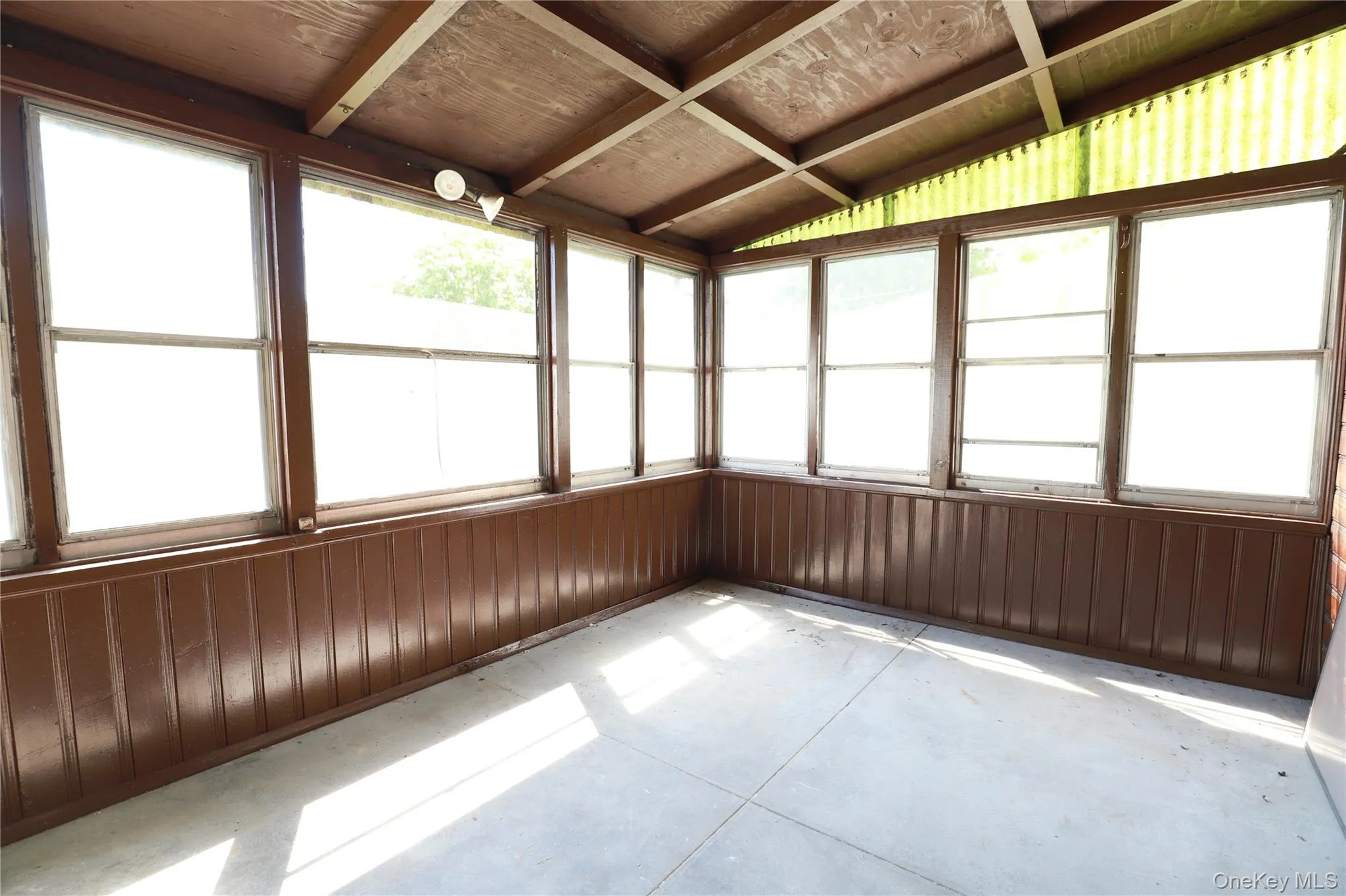 Enclosed porch with multiple pane windows, wood-paneled walls, exposed ceiling beams, and concrete flooring Enclosed porch with multiple pane windows, wood-paneled walls, exposed ceiling beams, and concrete flooring