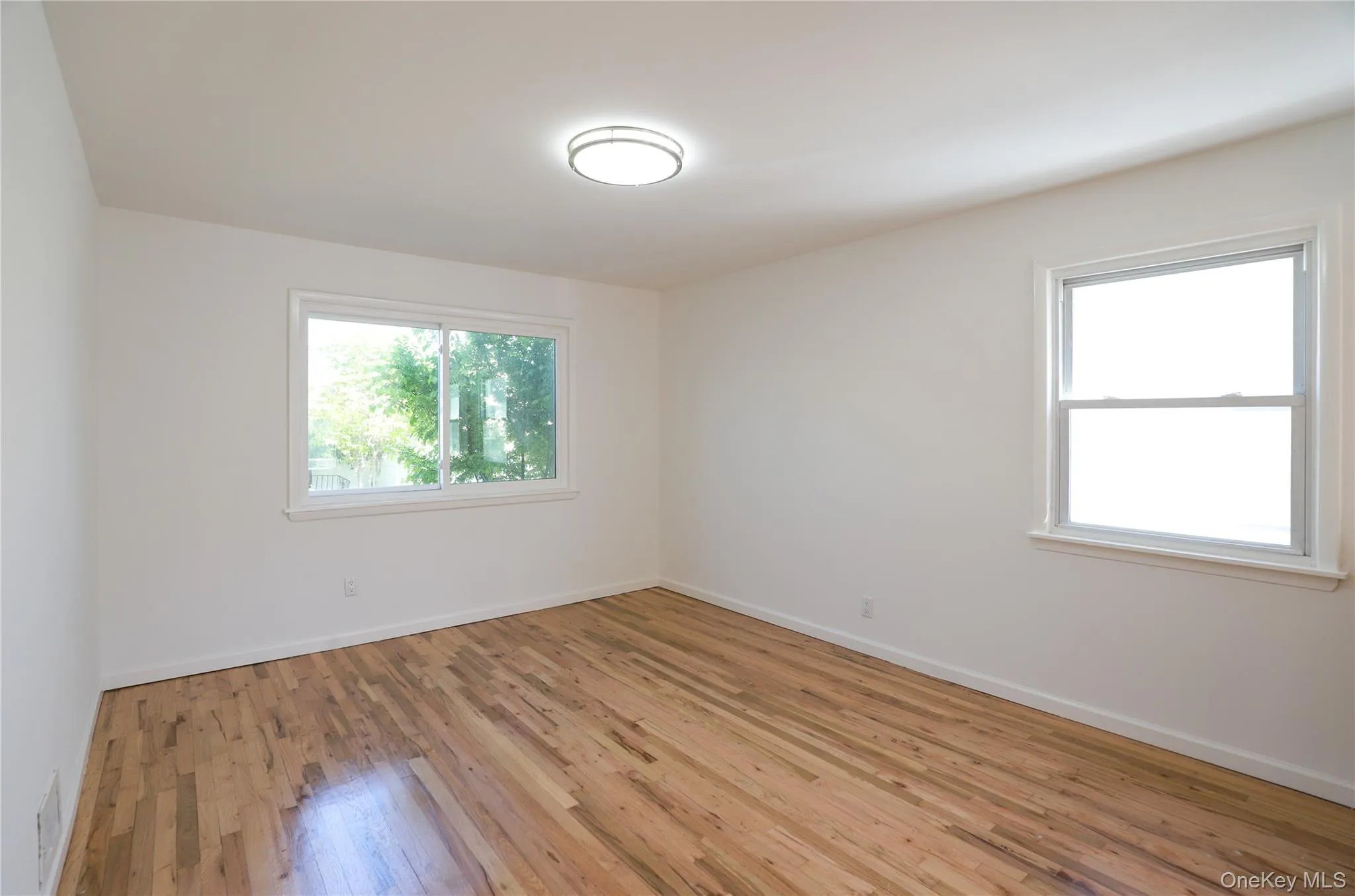 Room featuring wood-finish flooring, white walls, and a contemporary flush-mount ceiling light Room featuring wood-finish flooring, white walls, and a contemporary flush-mount ceiling light