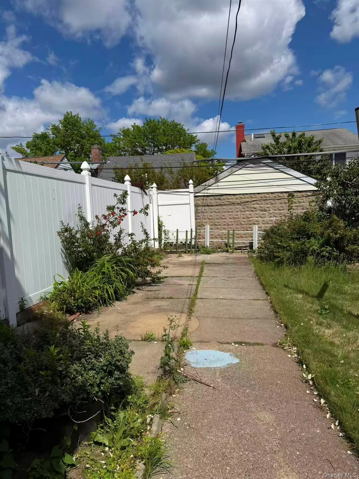 Paved concrete pathway bordered by a white vinyl fence and established greenery Paved concrete pathway bordered by a white vinyl fence and established greenery