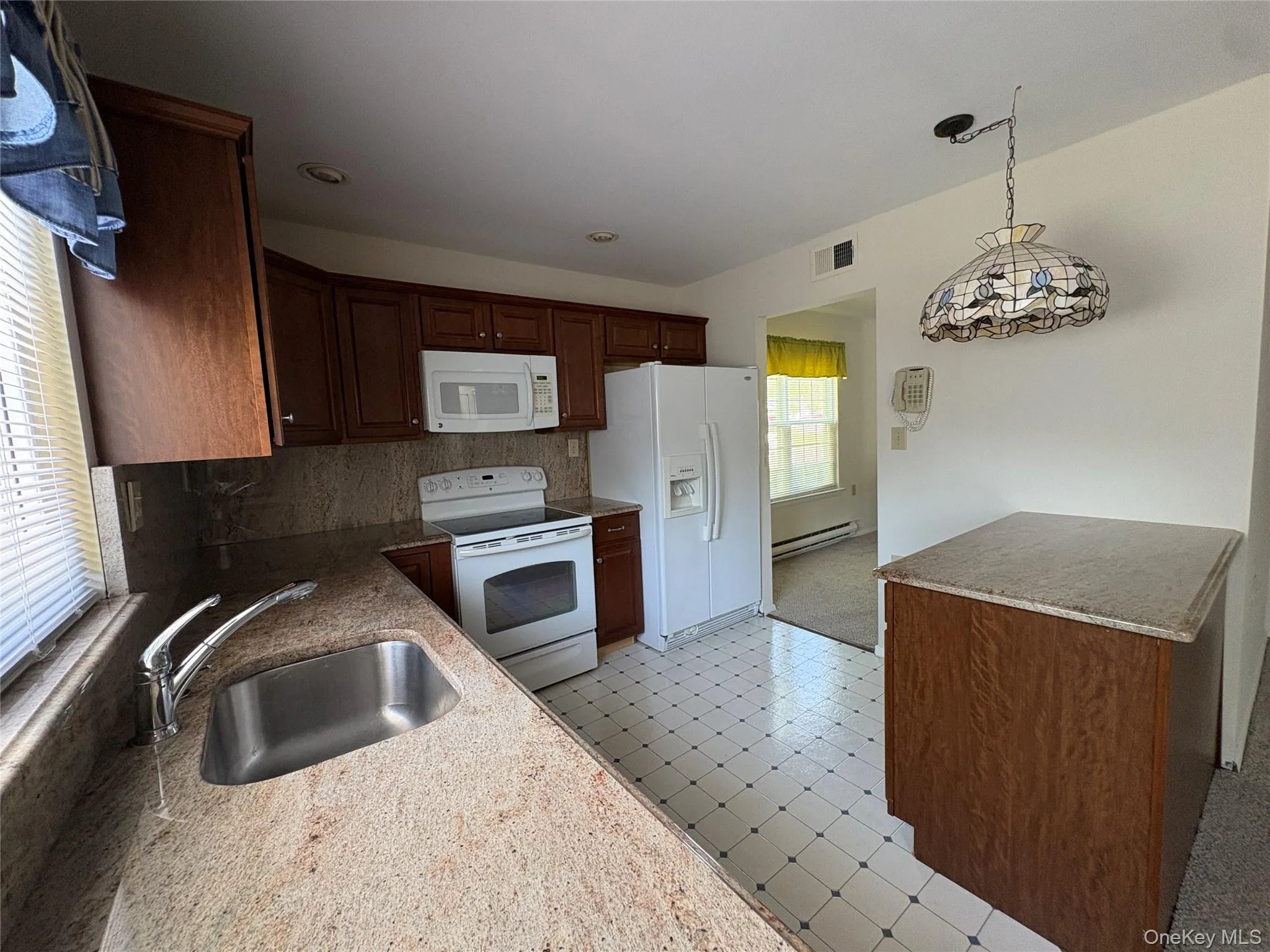 Kitchen featuring wood cabinetry, granite countertops, stainless steel sink with light filtering in from the window above and patterned floor tile. Kitchen featuring wood cabinetry, granite countertops, stainless steel sink with light filtering in from the window above and patterned floor tile.