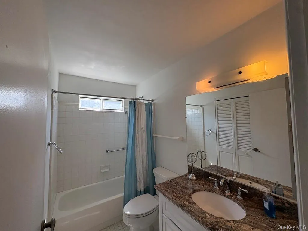 Bathroom featuring a granite- vanity an undermount sink, a large wall-mounted mirror, and a full bathtub with white tile surround. Bathroom featuring a granite- vanity an undermount sink, a large wall-mounted mirror, and a full bathtub with white tile surround.