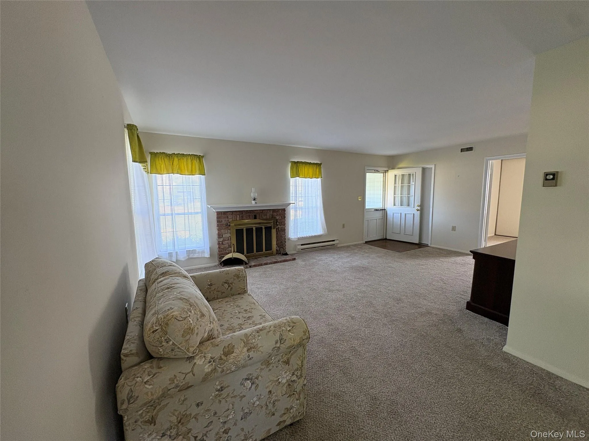 Spacious living area featuring neutral carpeting and a brick fireplace Spacious living area featuring neutral carpeting and a brick fireplace