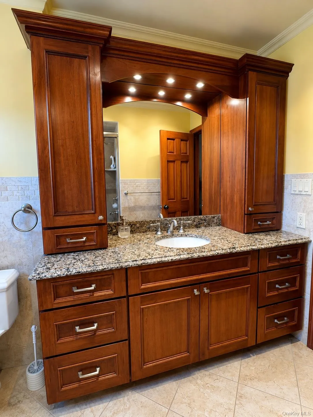 Custom vanity featuring cherry-toned cabinetry, granite countertop, undermount sink, and integrated overhead lighting Custom vanity featuring cherry-toned cabinetry, granite countertop, undermount sink, and integrated overhead lighting