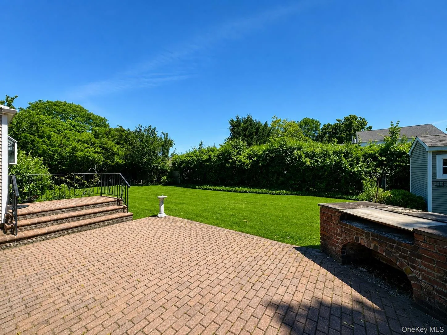 Expansive backyard featuring a large brick paver patio, a built-in brick outdoor cooking station, lush green lawn, and mature perimeter trees Expansive backyard featuring a large brick paver patio, a built-in brick outdoor cooking station, lush green lawn, and mature perimeter trees