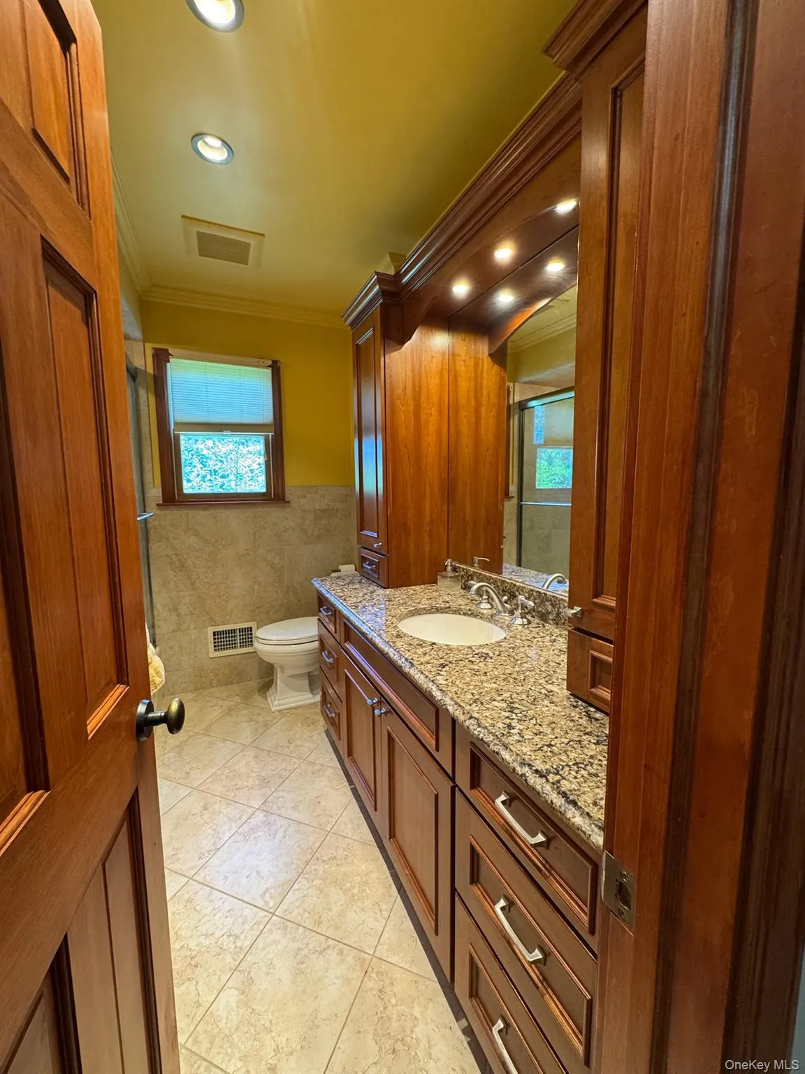 Bathroom featuring a wood-finish vanity with a light-toned stone countertop, an undermount sink, and polished chrome fixtures Bathroom featuring a wood-finish vanity with a light-toned stone countertop, an undermount sink, and polished chrome fixtures