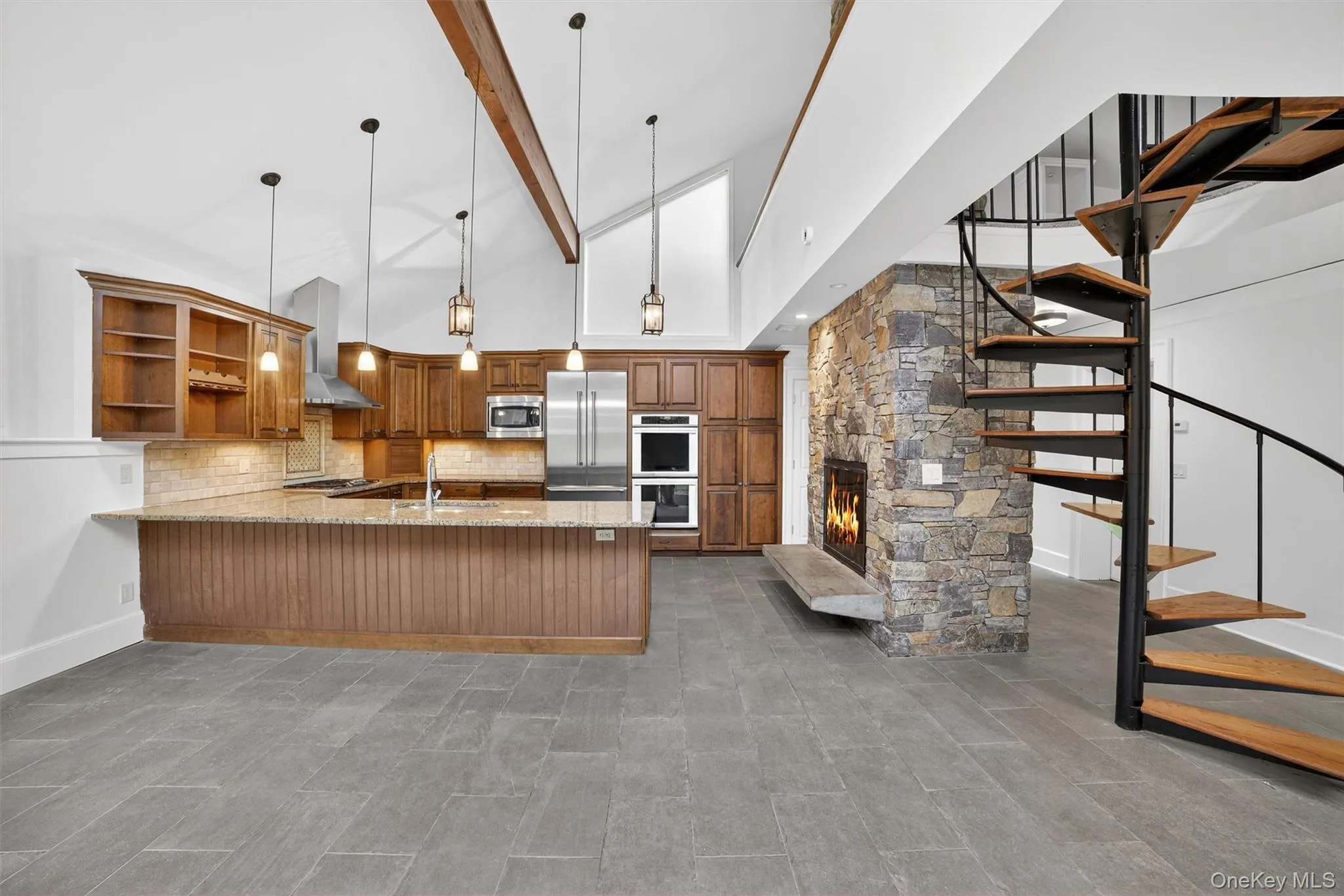 Kitchen with built in appliances, wall chimney range hood, open shelves, brown cabinetry, and a peninsula Kitchen with built in appliances, wall chimney range hood, open shelves, brown cabinetry, and a peninsula