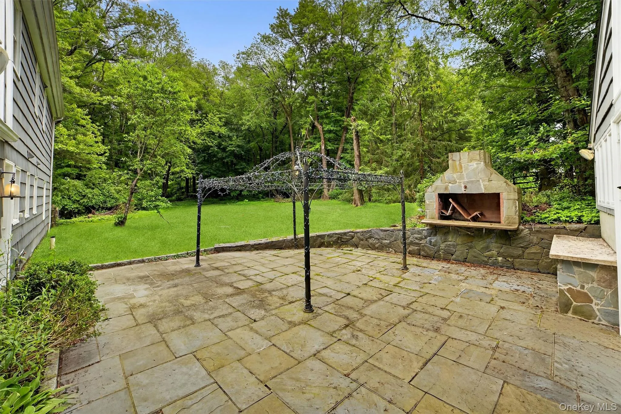 View of patio featuring an outdoor stone fireplace and view of wooded area View of patio featuring an outdoor stone fireplace and view of wooded area