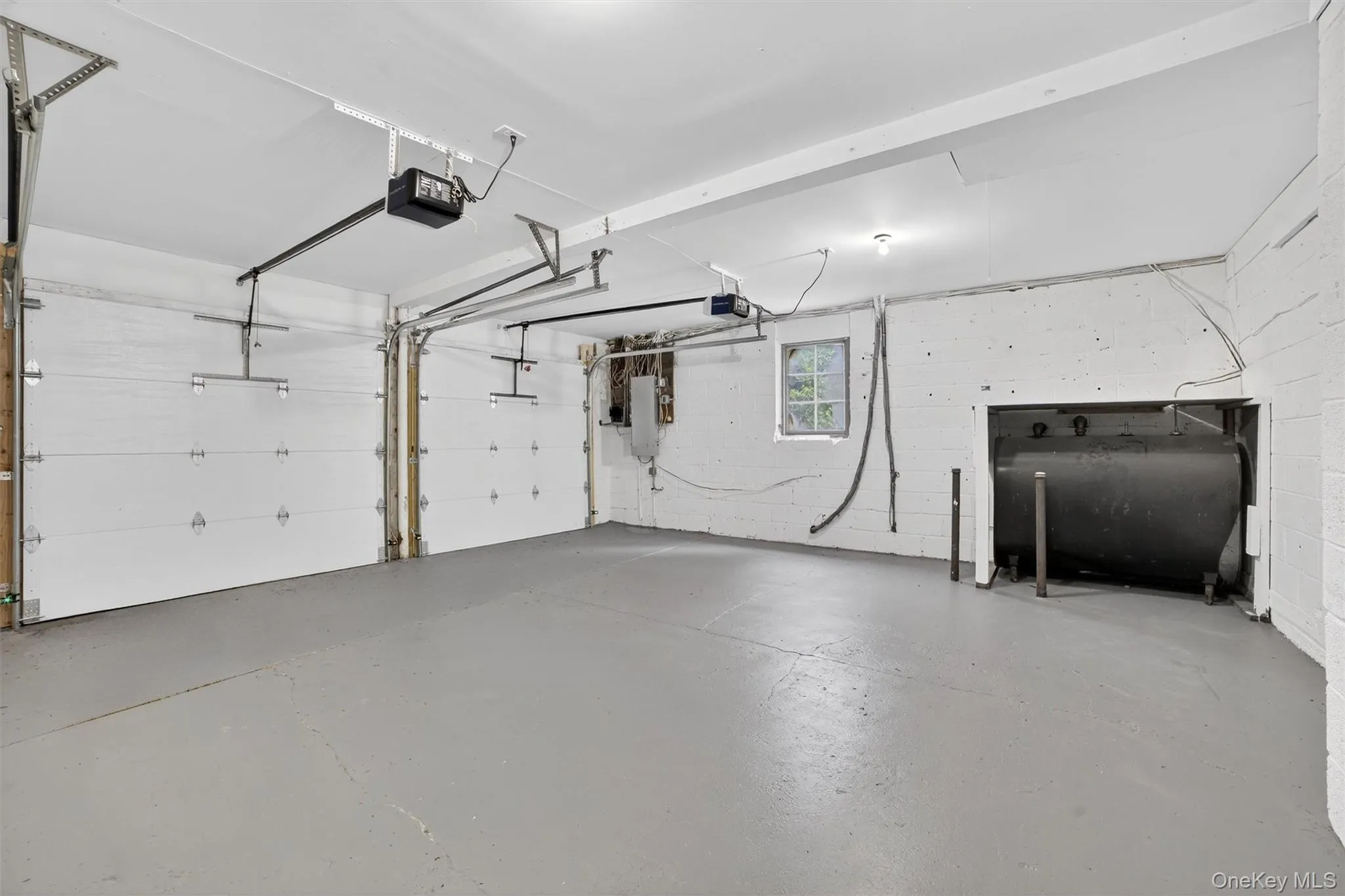 Garage with oil tank, concrete block wall, a garage door opener, and electric panel Garage with oil tank, concrete block wall, a garage door opener, and electric panel