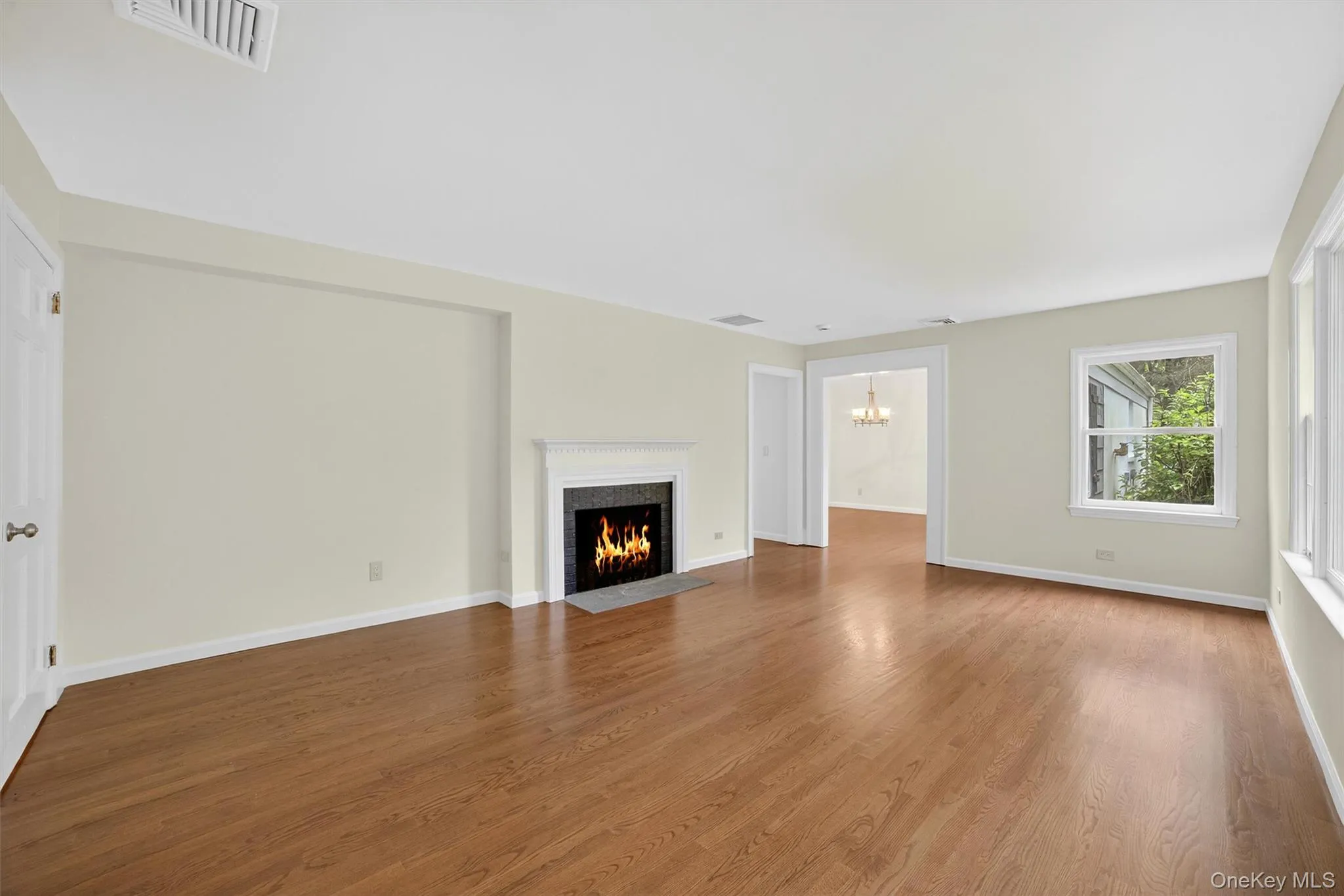 Unfurnished living room featuring a chandelier, a fireplace with flush hearth, and wood finished floors Unfurnished living room featuring a chandelier, a fireplace with flush hearth, and wood finished floors