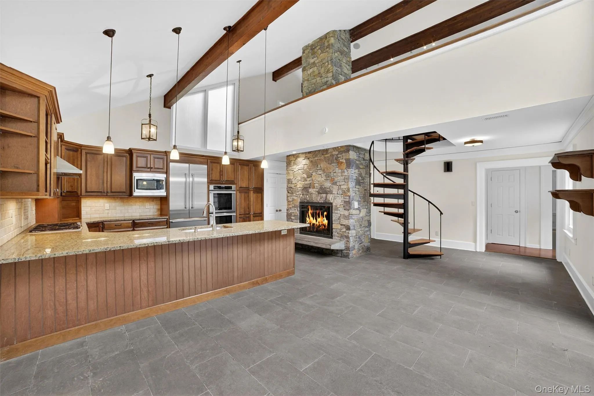 Kitchen featuring built in appliances, a stone fireplace, light stone counters, open floor plan, and a peninsula Kitchen featuring built in appliances, a stone fireplace, light stone counters, open floor plan, and a peninsula
