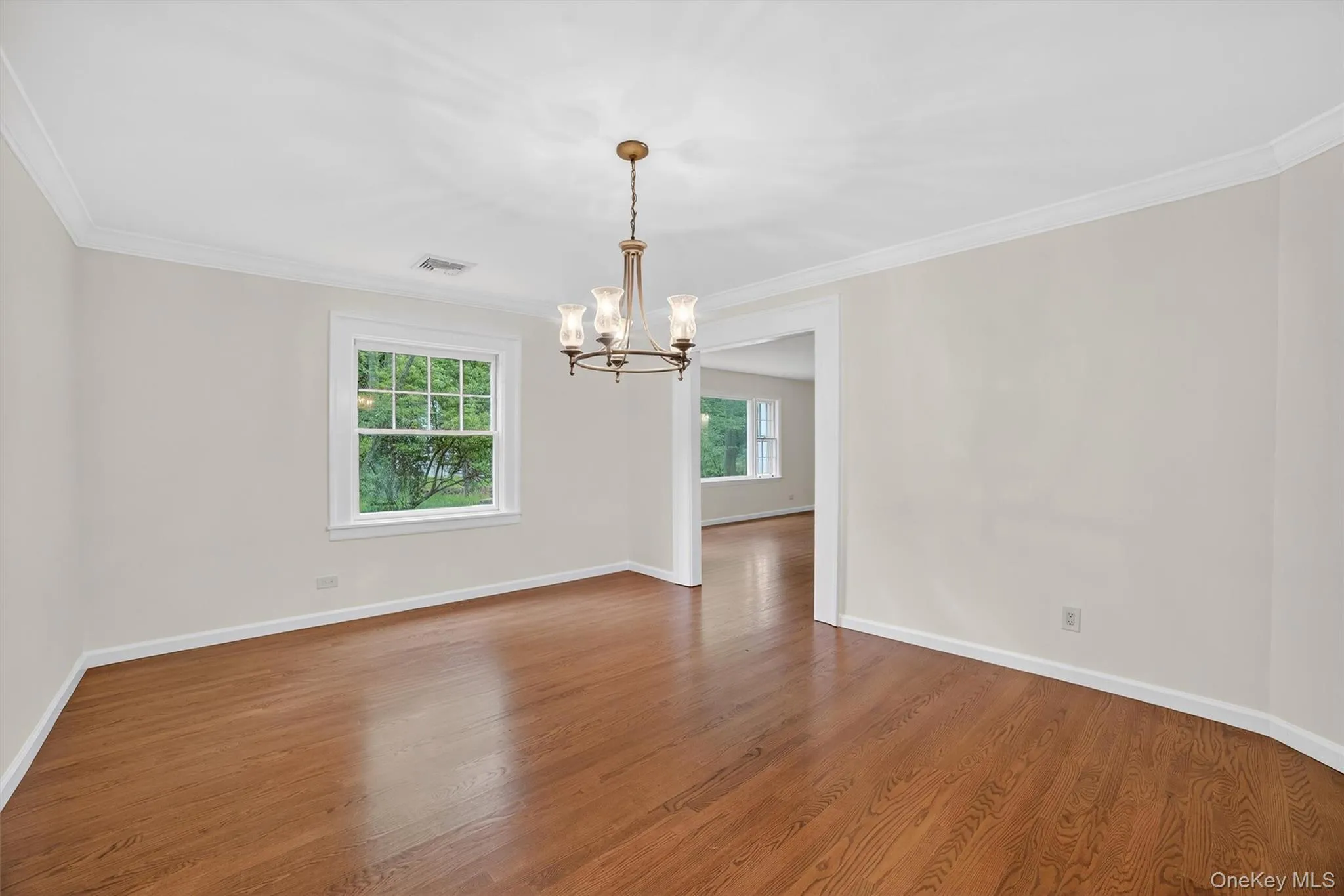 Empty room with a chandelier, wood finished floors, and crown molding Empty room with a chandelier, wood finished floors, and crown molding