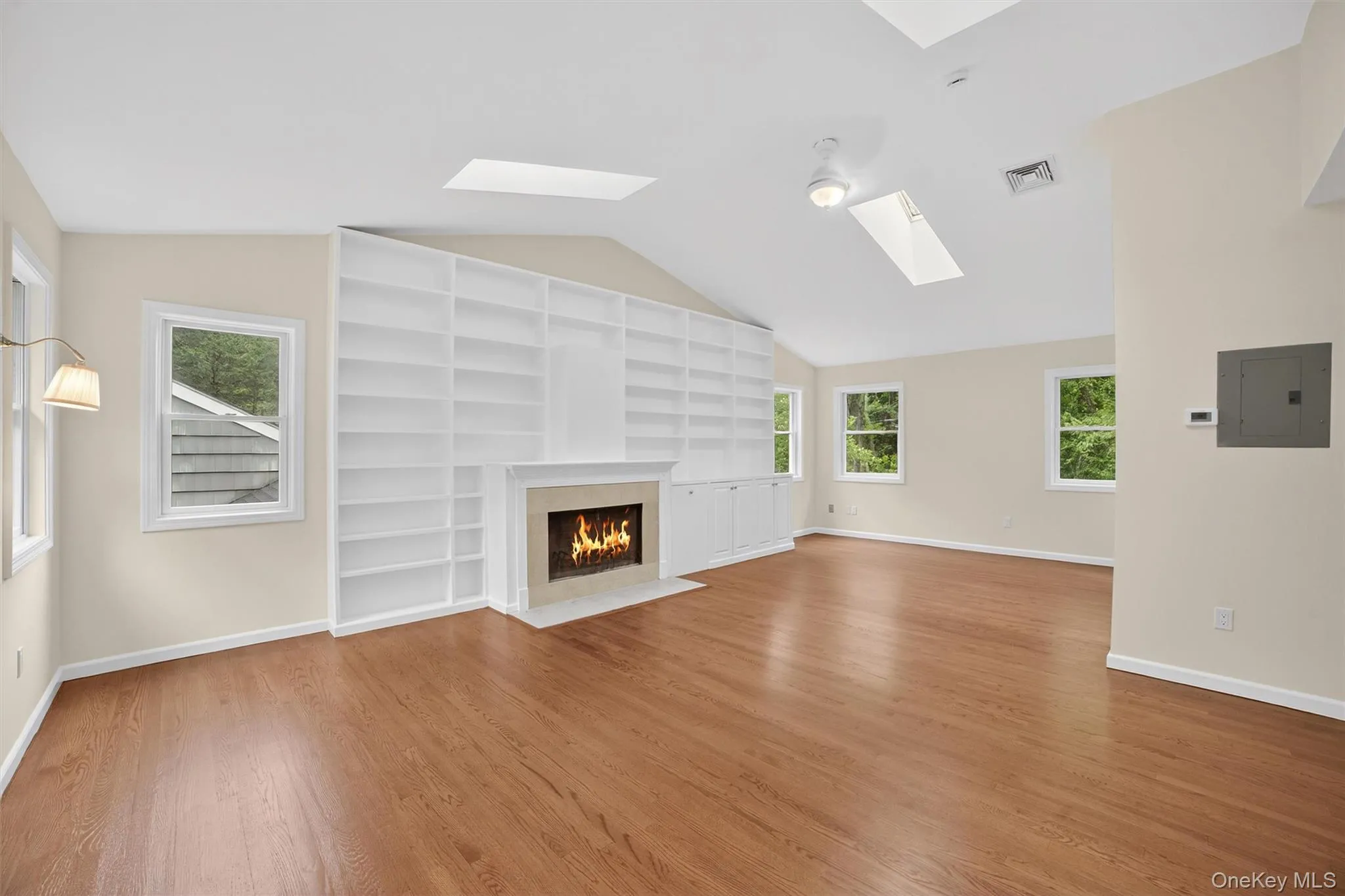 Unfurnished living room with a skylight, lofted ceiling, electric panel, wood finished floors, and a fireplace Unfurnished living room with a skylight, lofted ceiling, electric panel, wood finished floors, and a fireplace
