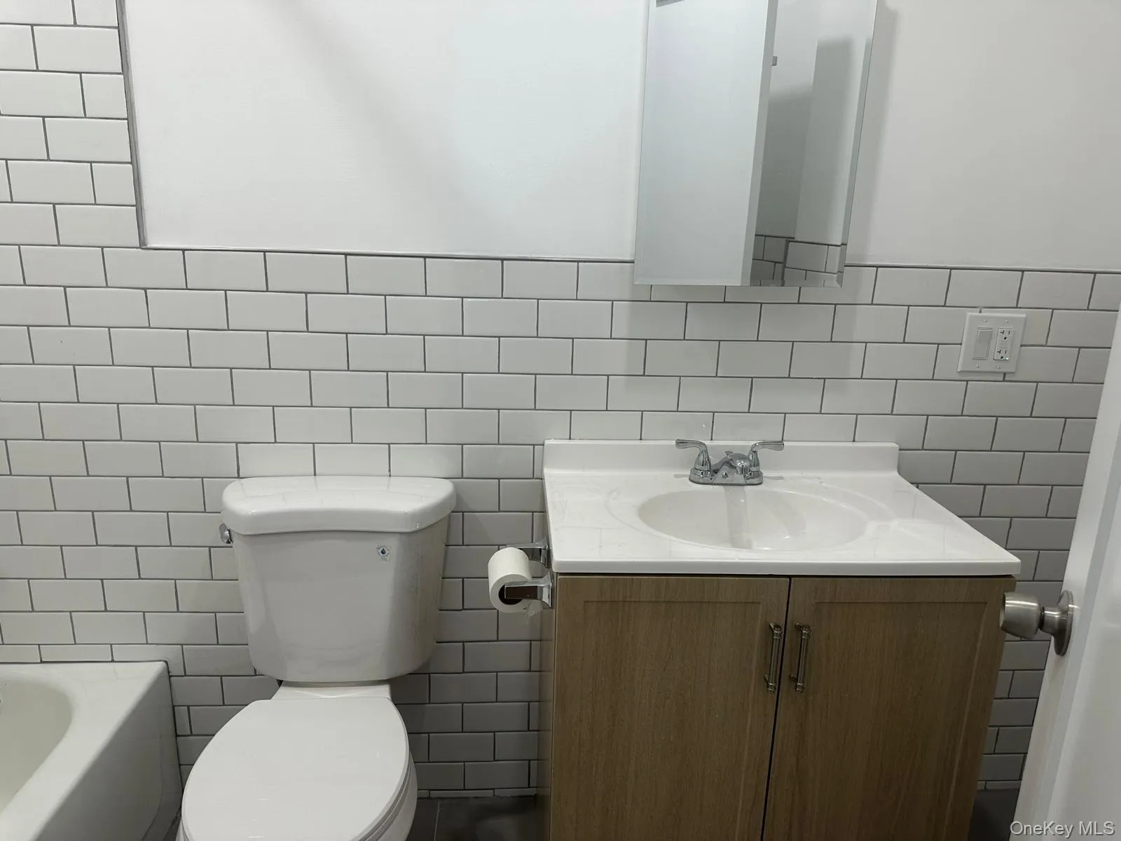 Bathroom featuring subway tile walls, a white porcelain toilet, and a wood-finish vanity with an integrated sink Bathroom featuring subway tile walls, a white porcelain toilet, and a wood-finish vanity with an integrated sink