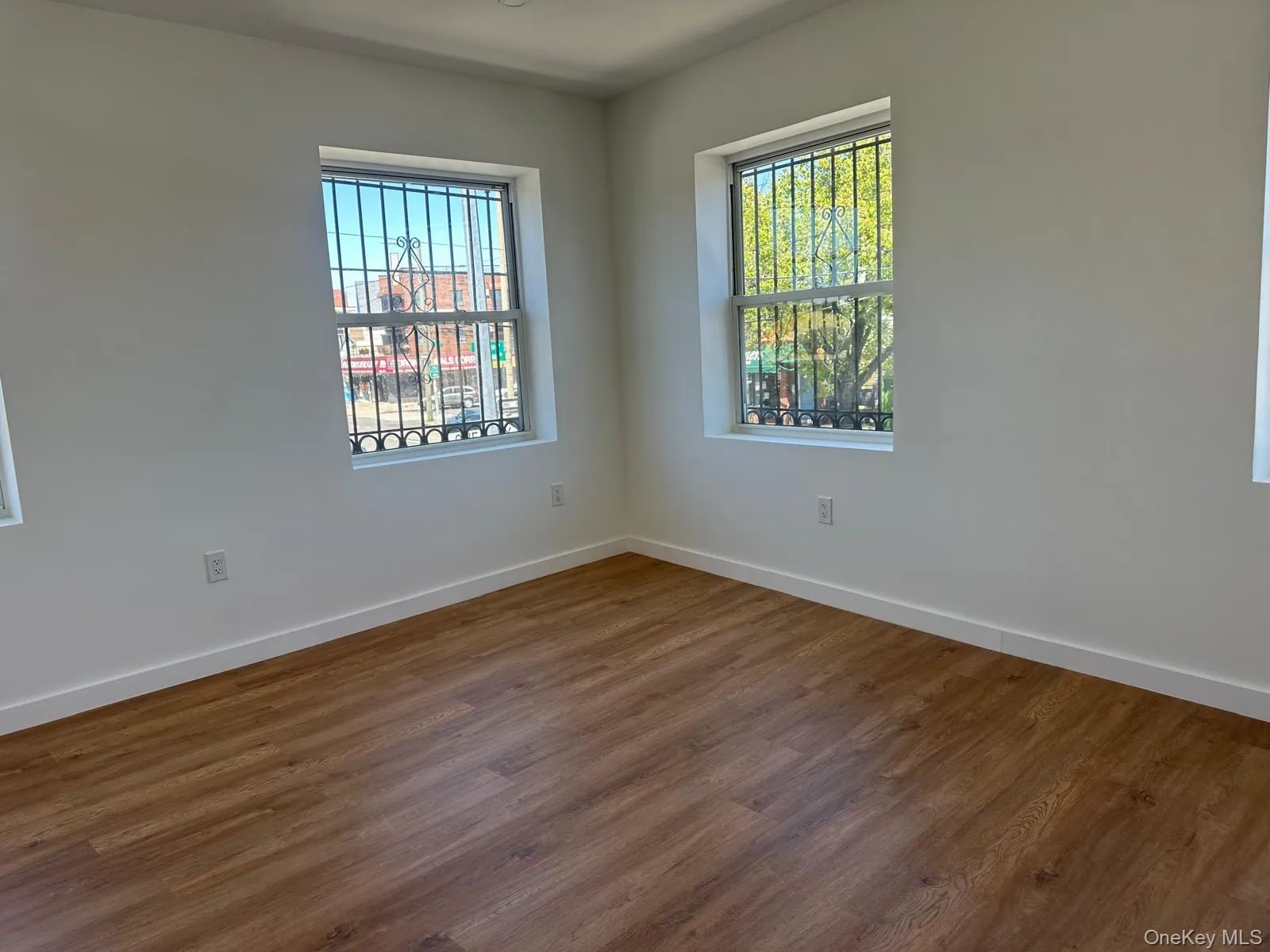 Spacious room with wood-finish flooring, white baseboards, and bright white walls Spacious room with wood-finish flooring, white baseboards, and bright white walls