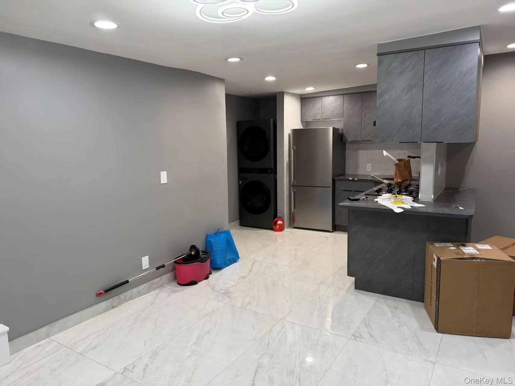 Kitchen with dark countertops, recessed lighting, a peninsula, freestanding refrigerator, and gray cabinetry Kitchen with dark countertops, recessed lighting, a peninsula, freestanding refrigerator, and gray cabinetry