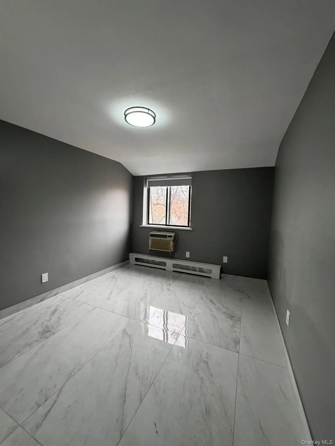 Spare room with light marble finish floors, a baseboard radiator, lofted ceiling, and a wall mounted air conditioner Spare room with light marble finish floors, a baseboard radiator, lofted ceiling, and a wall mounted air conditioner