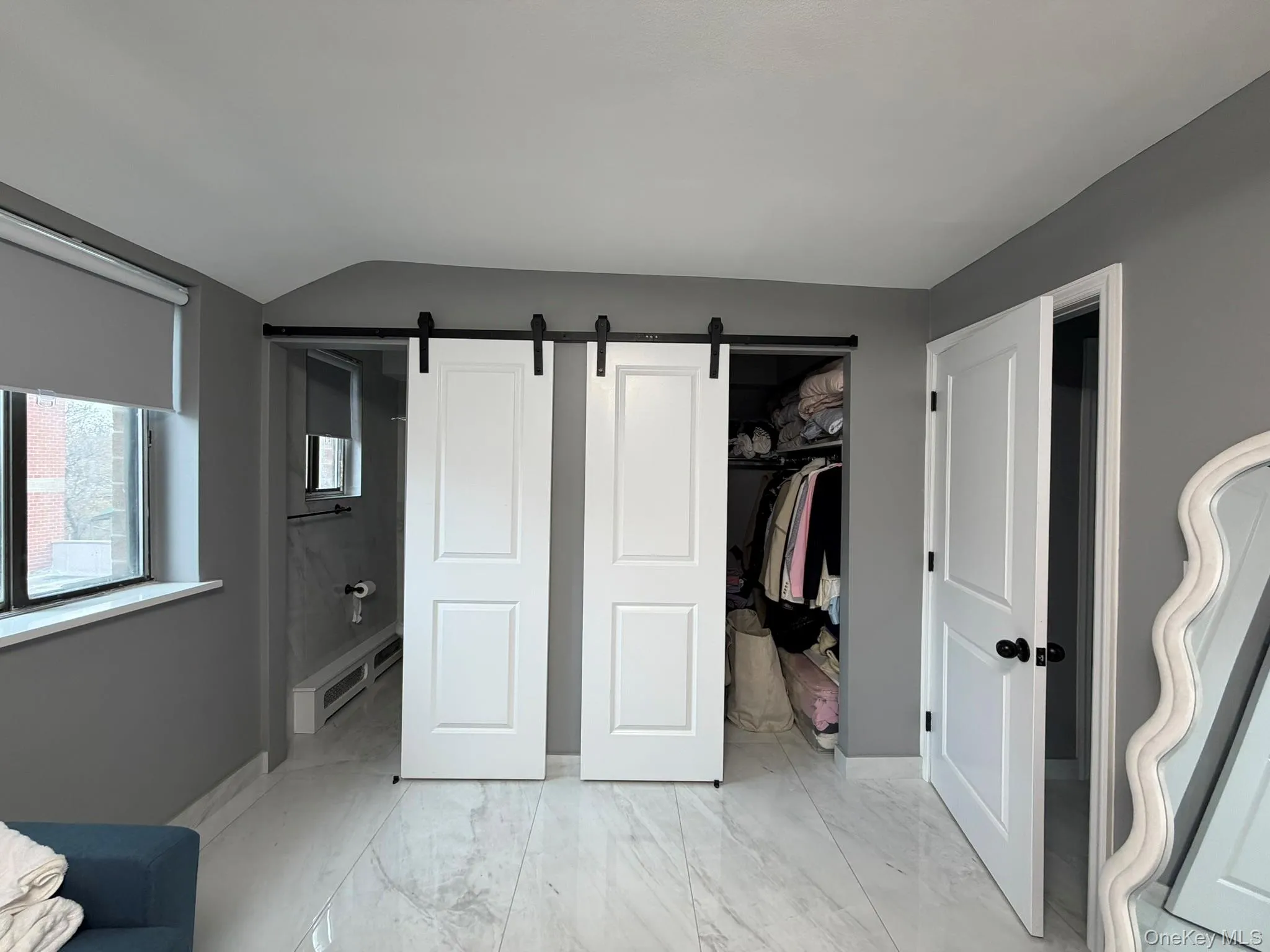 Bedroom with a barn door, light marble finish flooring, ensuite bathroom, a spacious closet, and a baseboard heating unit Bedroom with a barn door, light marble finish flooring, ensuite bathroom, a spacious closet, and a baseboard heating unit