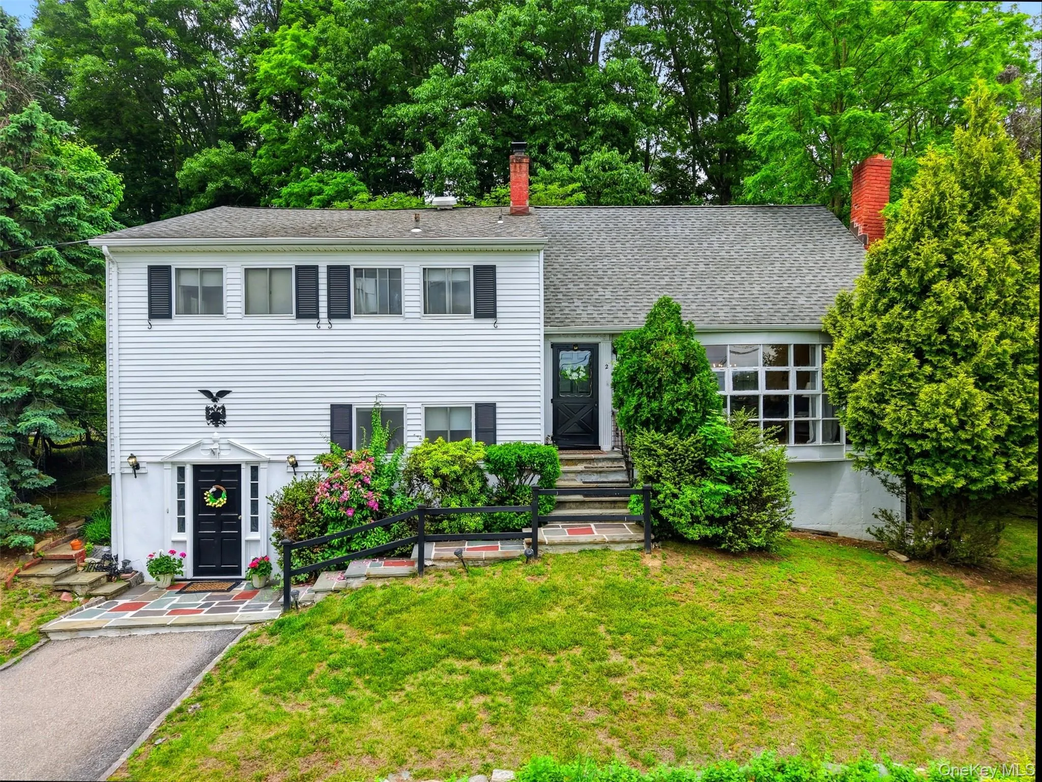 Colonial-style residence featuring white siding, black shutters, and featuring a multi-level design with black shutters and a prominent bay window Colonial-style residence featuring white siding, black shutters, and featuring a multi-level design with black shutters and a prominent bay window